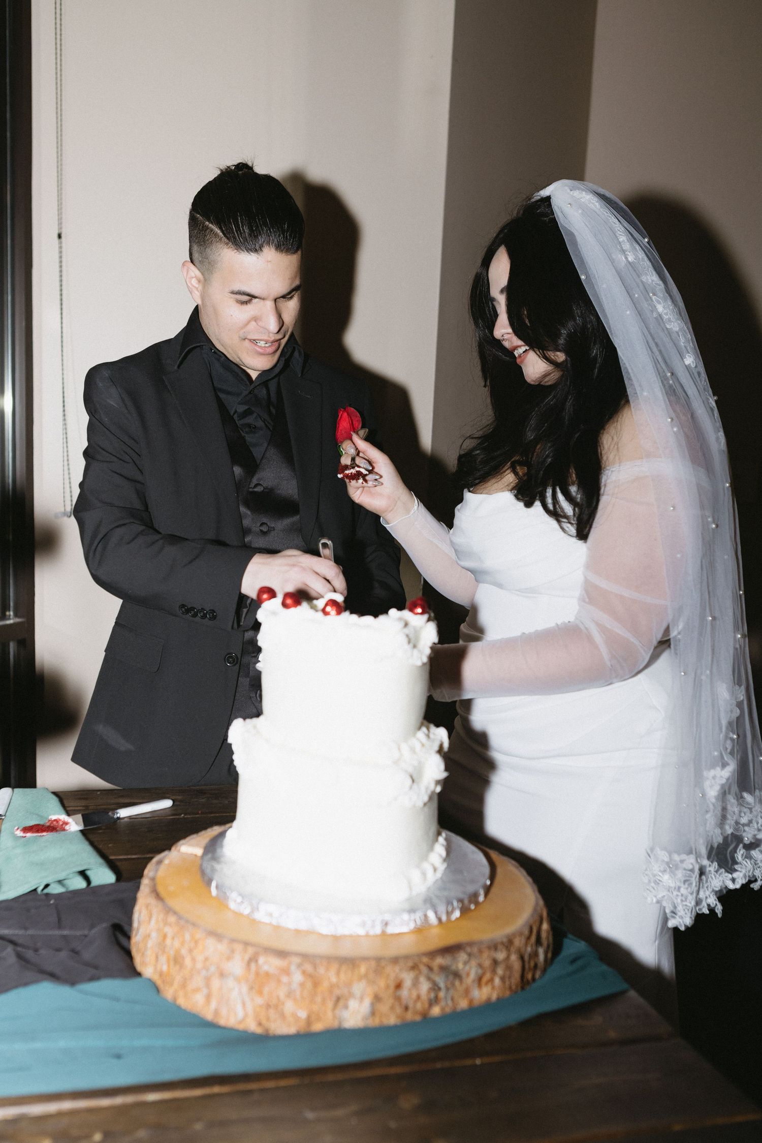 A couple cutting their white wedding cake together on a wooden cake stand during their reception.
