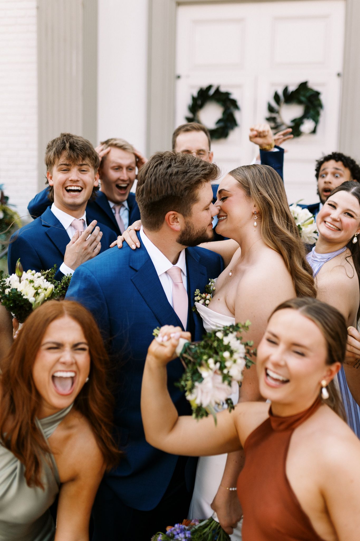 Joyful wedding party celebration with bridesmaids and groomsmen in blue suits.
