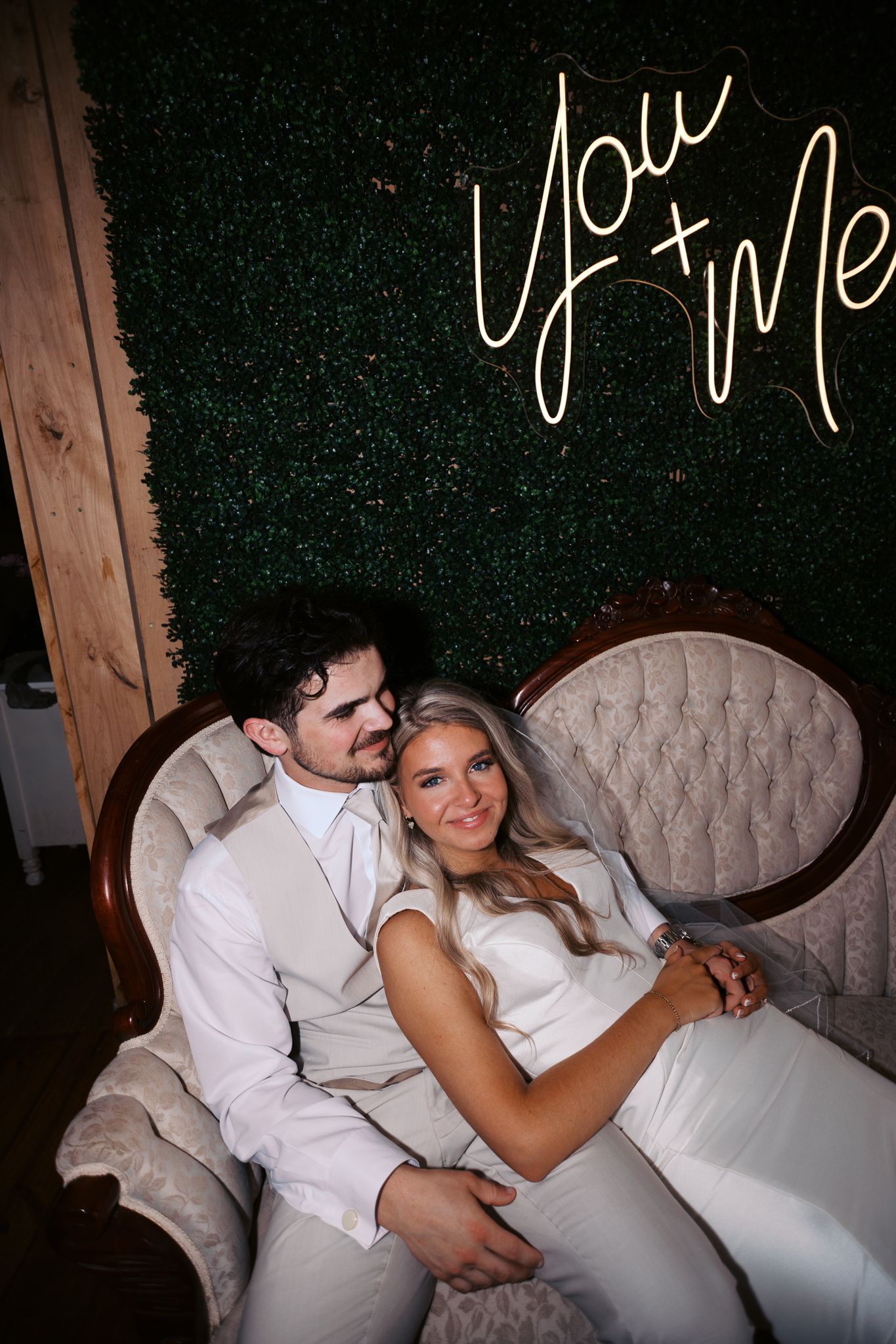 A couple in white attire sharing intimate moments on an elegant tufted sofa at an event.