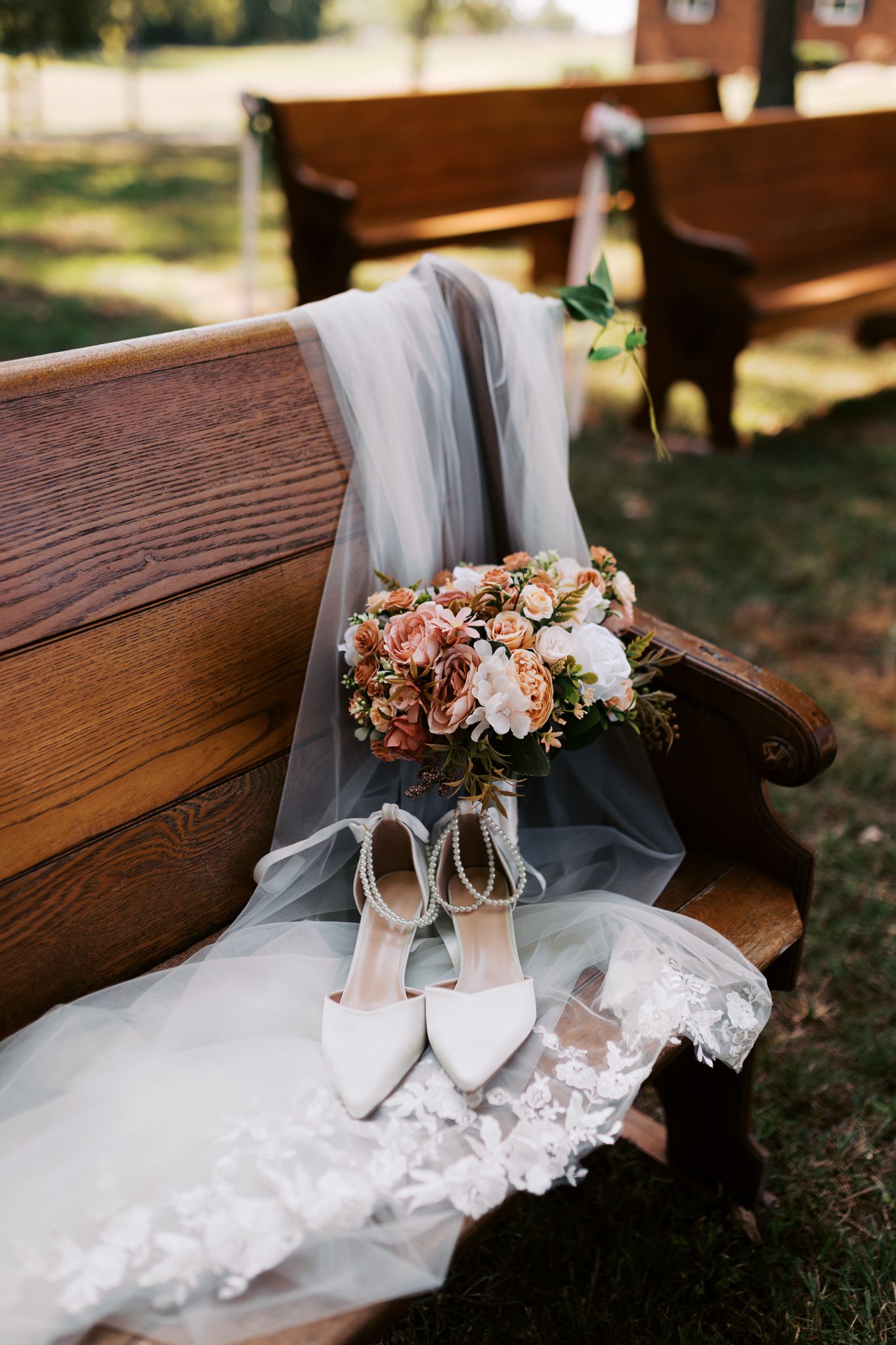 White bridal shoes and veil decorated with floral arrangements on a wooden church pew.