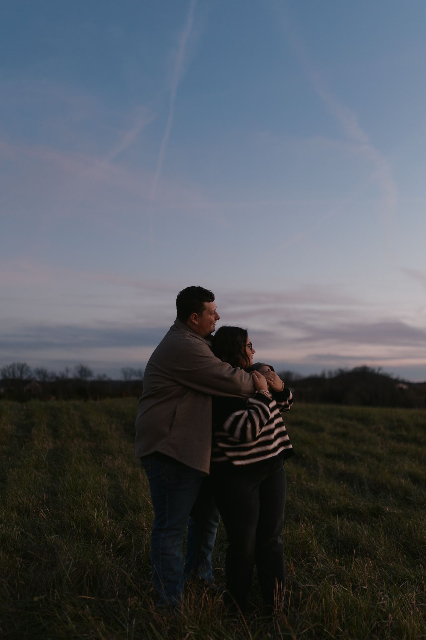Couple embracing while watching sunset in a countryside field.