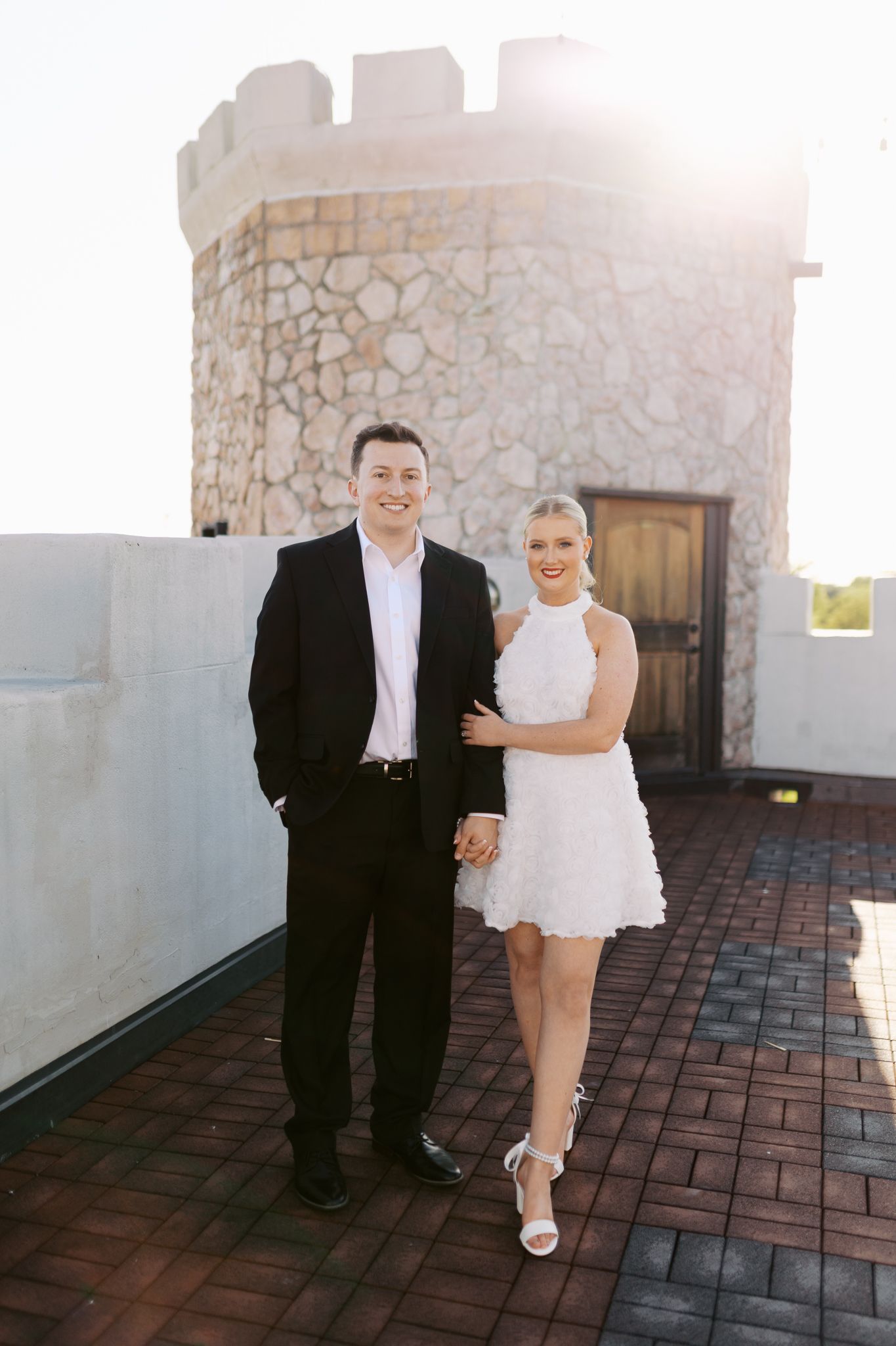 Couple posing together on castle tower balcony during sunset.