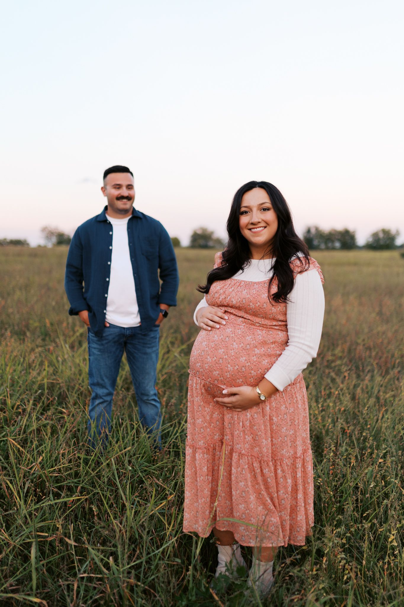 A maternity photoshoot in a field with a person in a floral dress showing their baby bump.