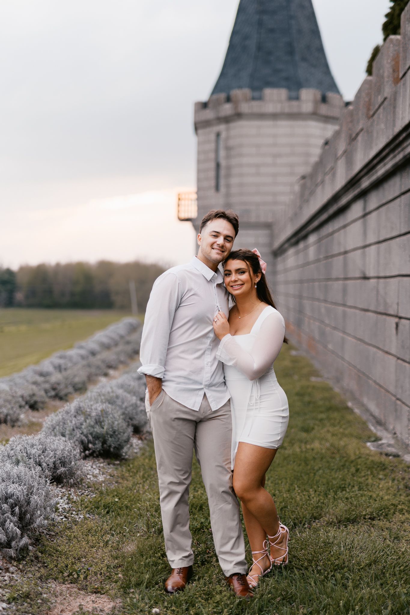 Couple in white outfits posing together near castle tower at sunset.