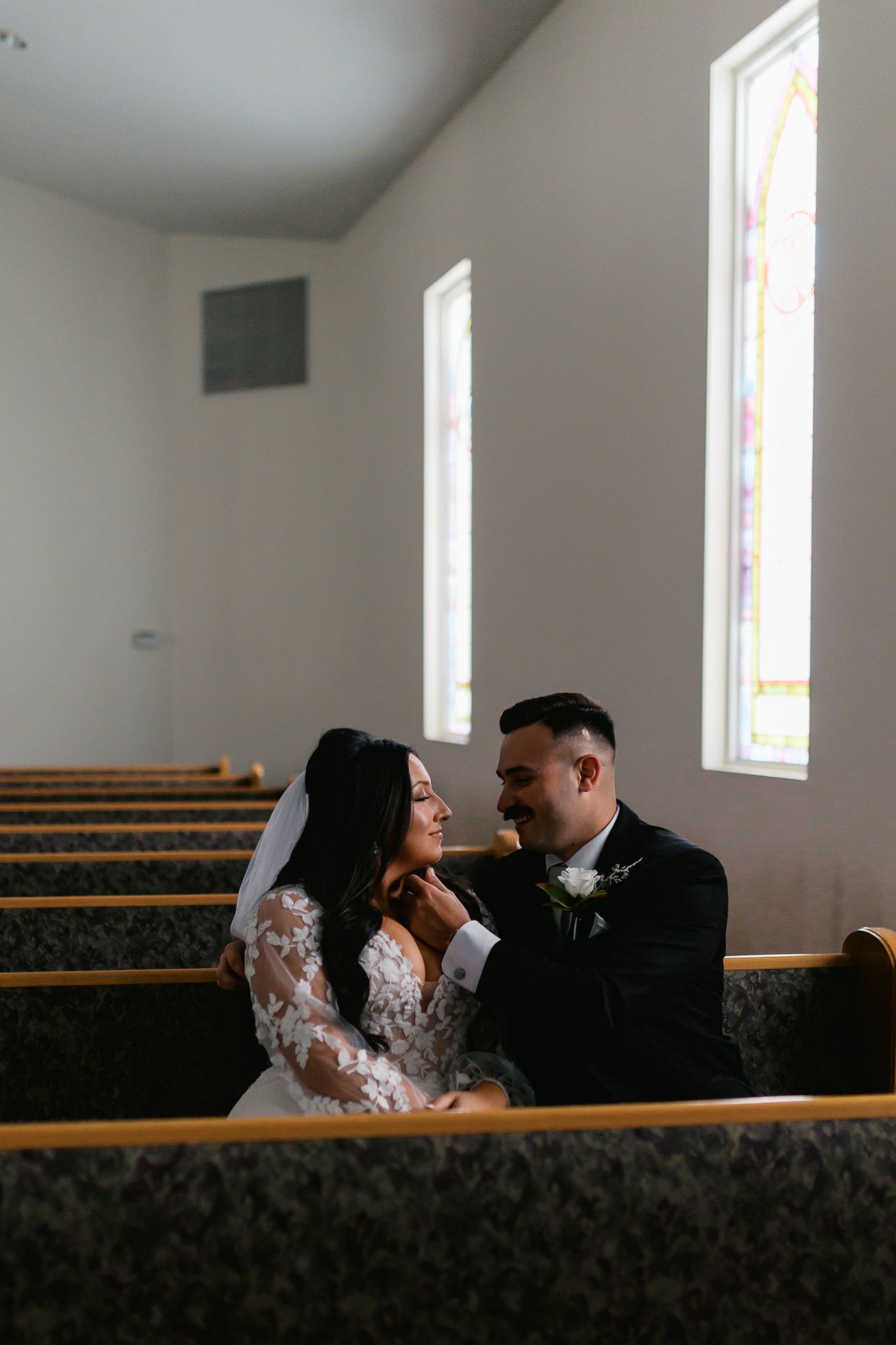 A couple shares a tender moment in a church pew with natural light streaming through windows.