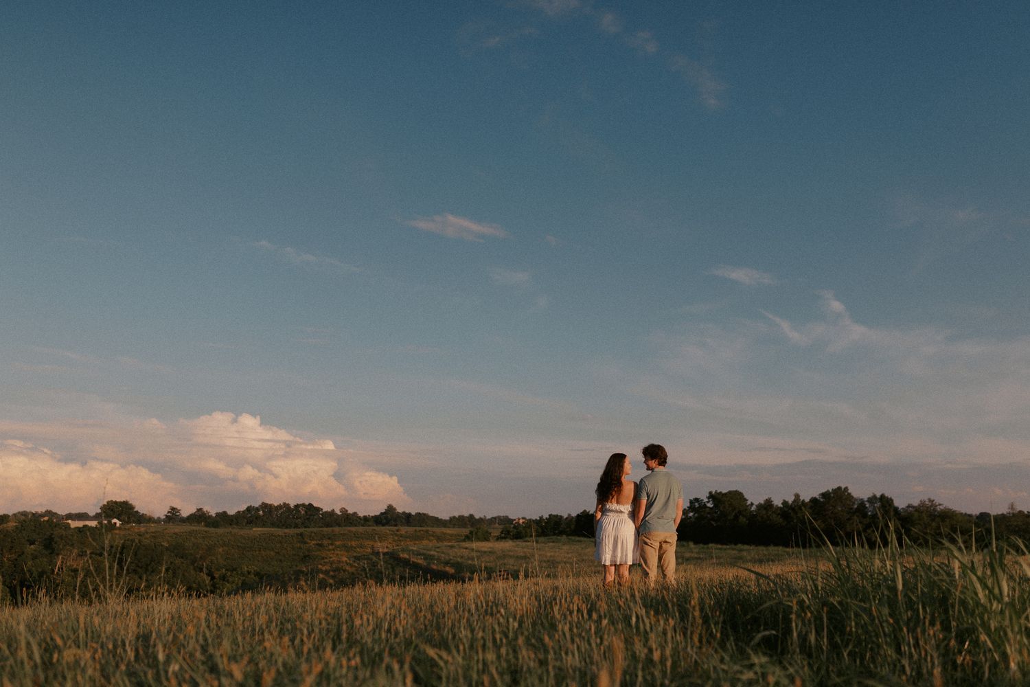 Silhouetted couple standing in field during golden sunset.