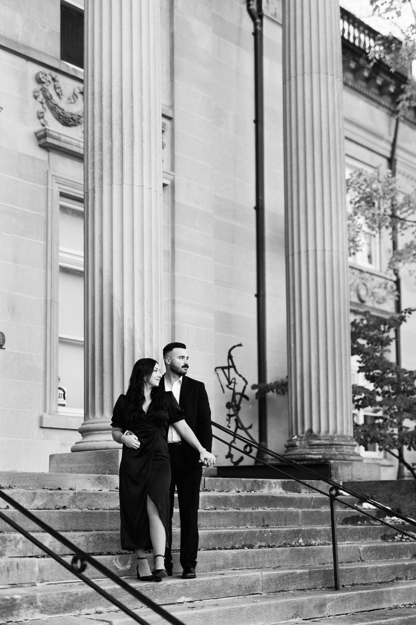 A romantic black and white photo of a couple standing on grand stone steps between classic columns.