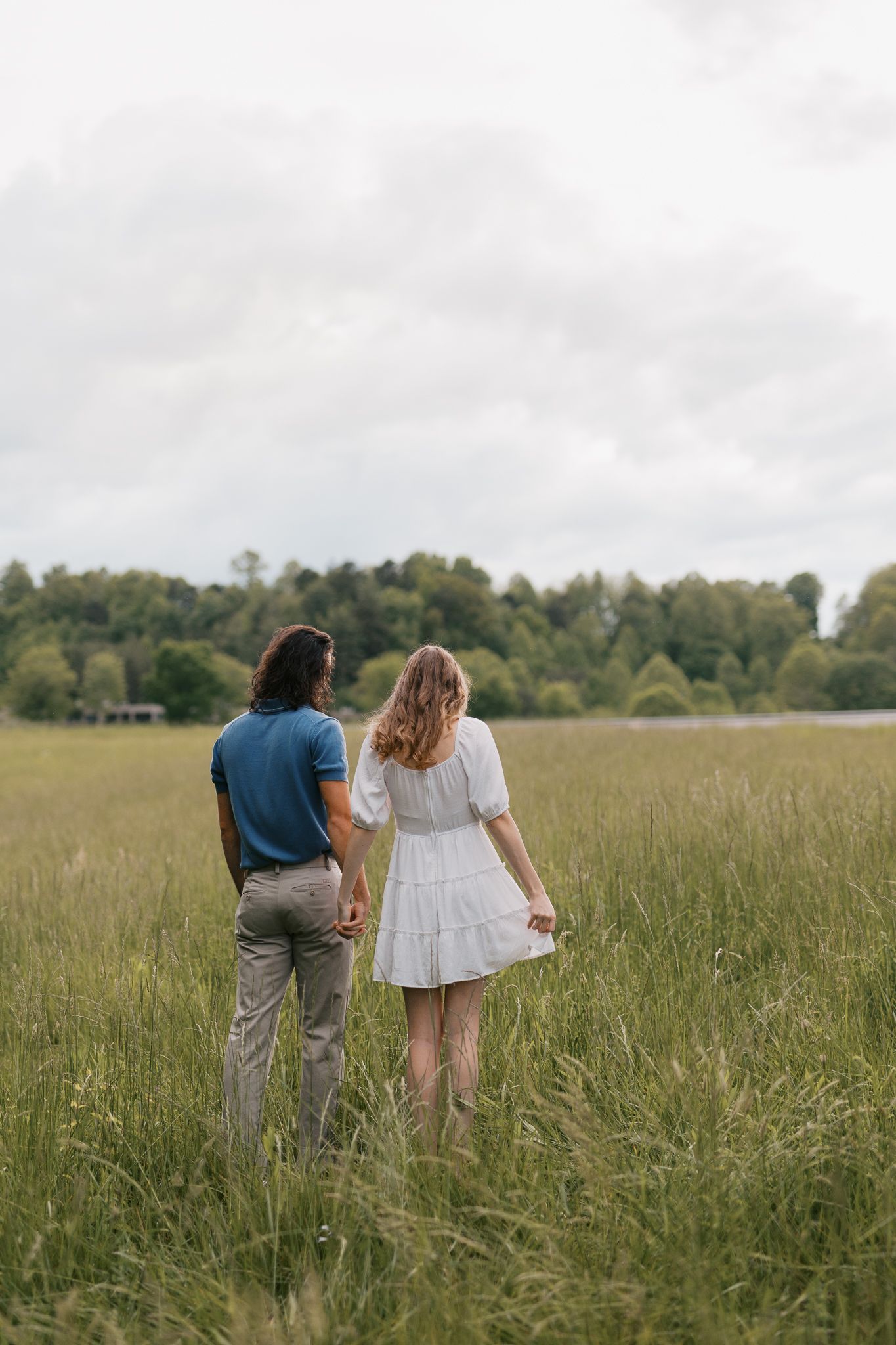 Couple holding hands while standing in a serene meadow on an overcast day.