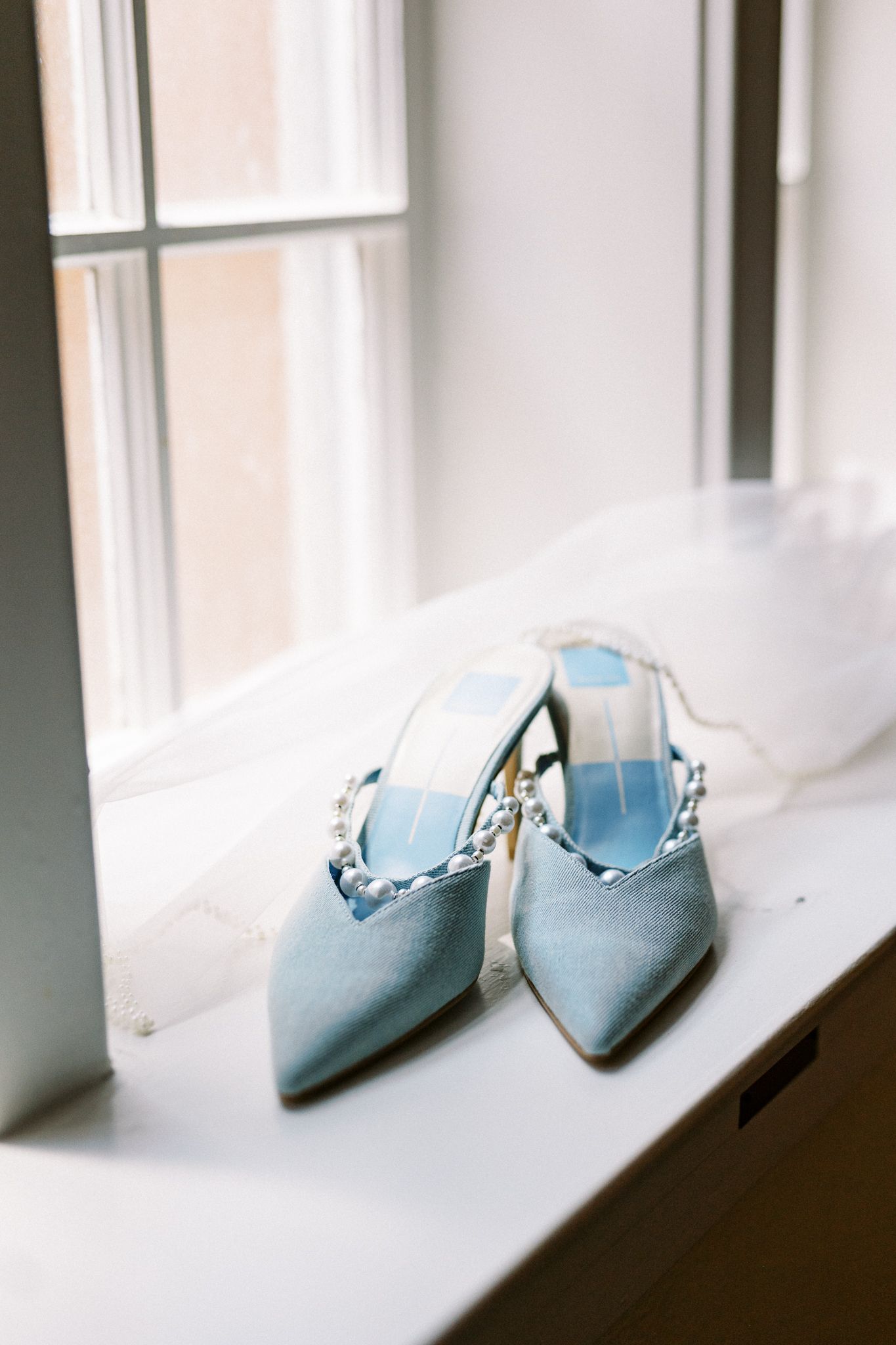 Light blue ballet flats arranged artistically on a white windowsill in natural light.