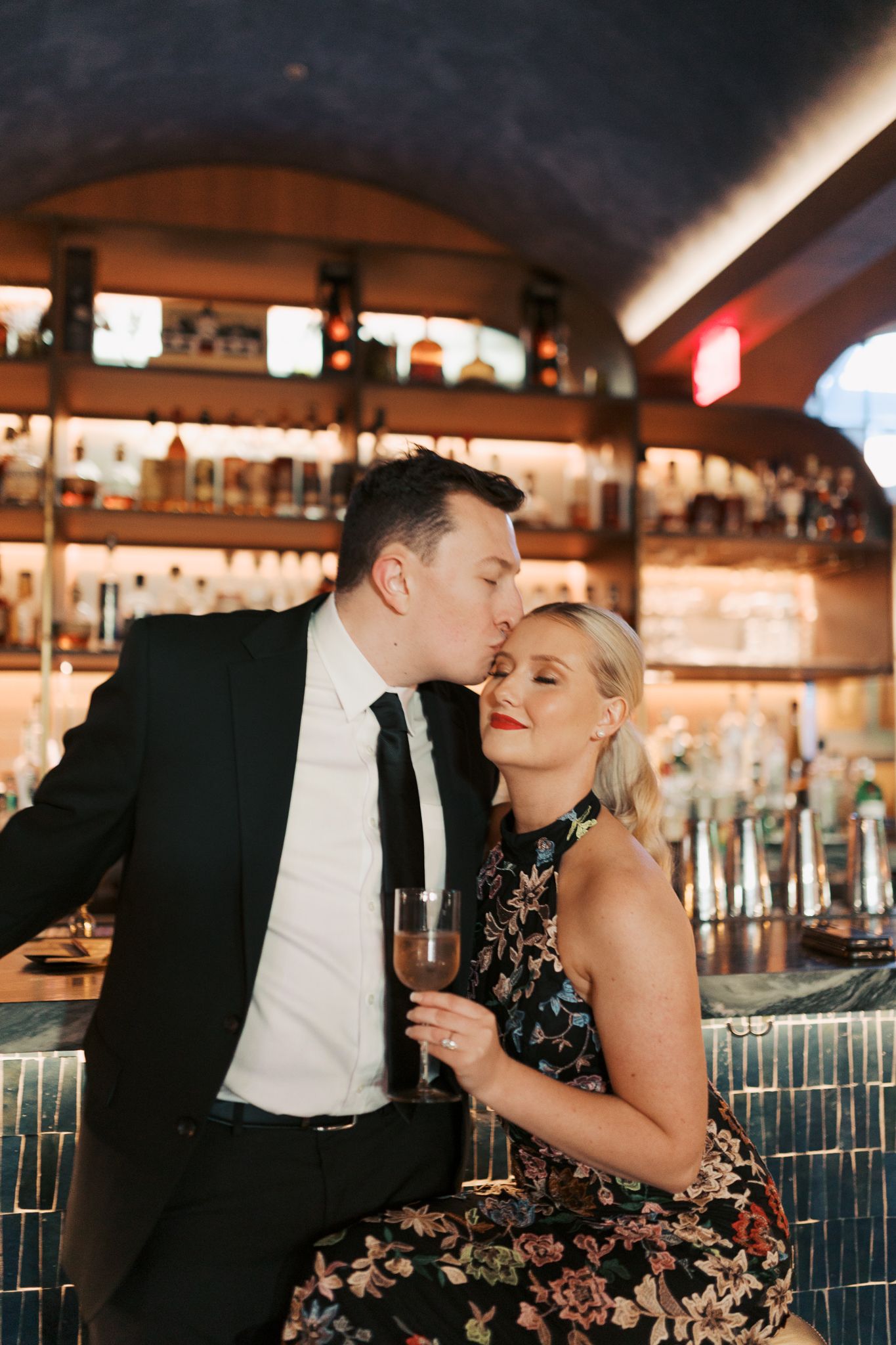 Elegant couple sharing an intimate moment at a luxurious bar with ambient lighting.
