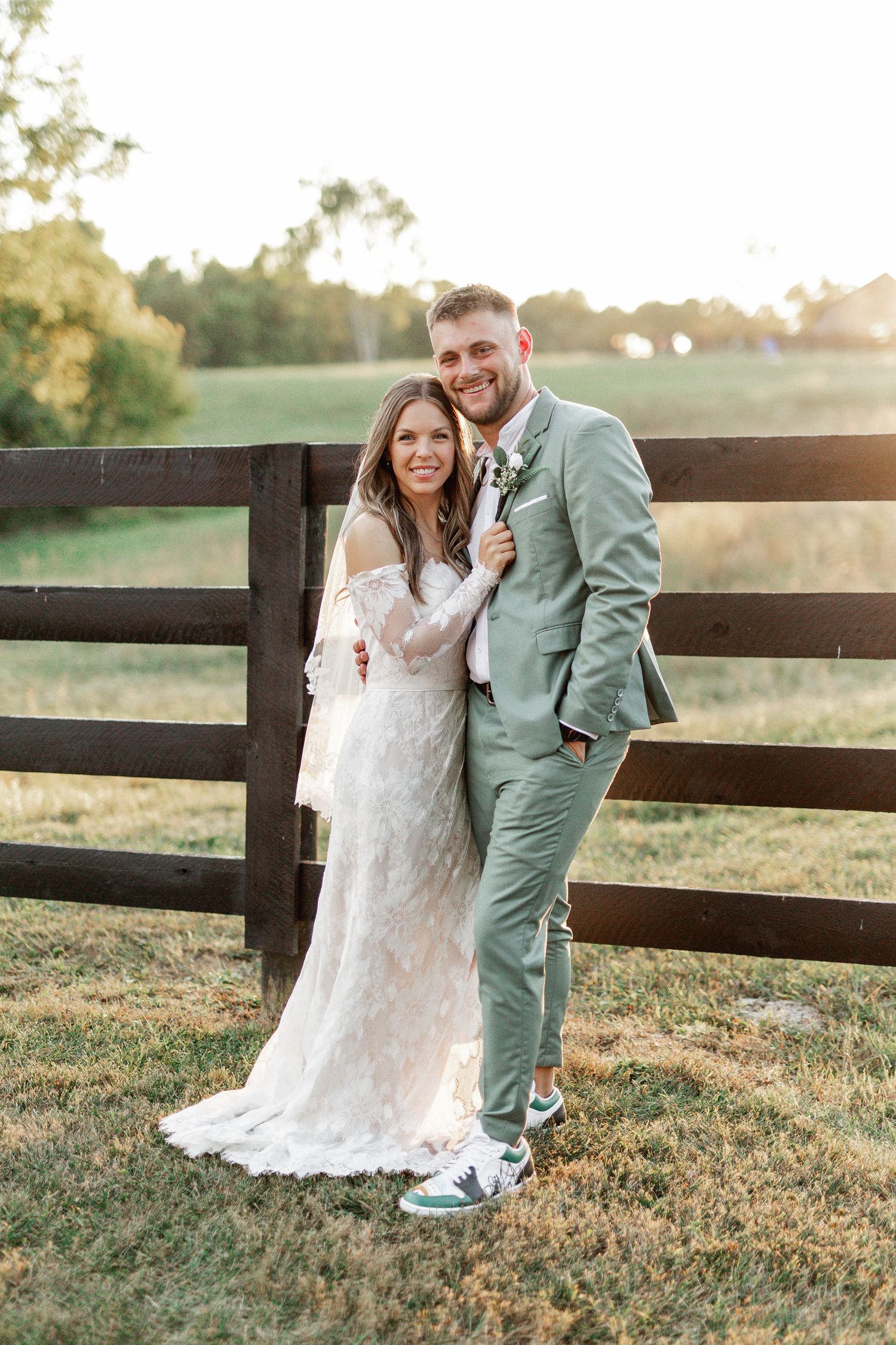 Couple in wedding attire sharing intimate moments by wooden fence at sunset.