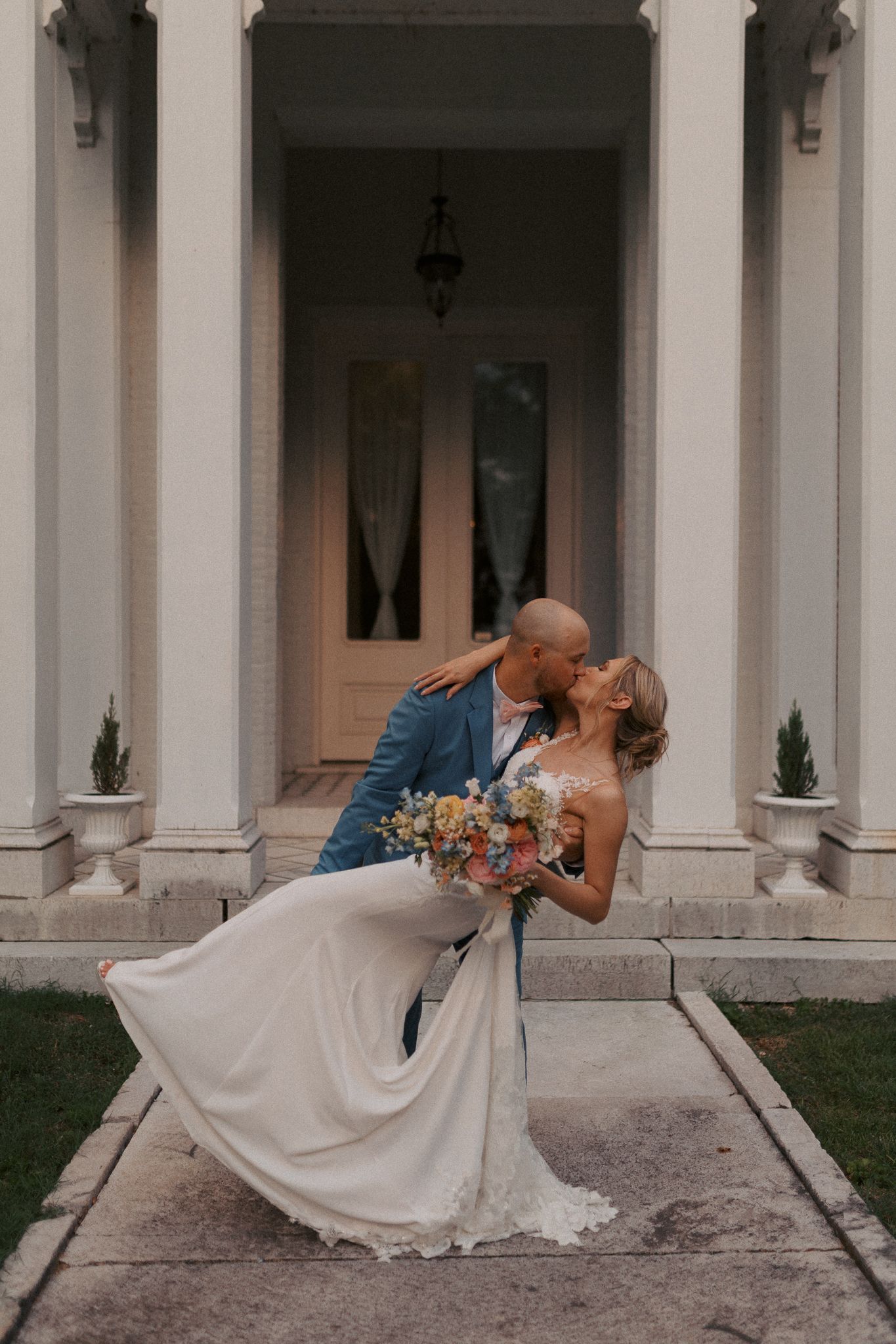 A wedding couple shares an intimate dip pose in front of a classical columned building.