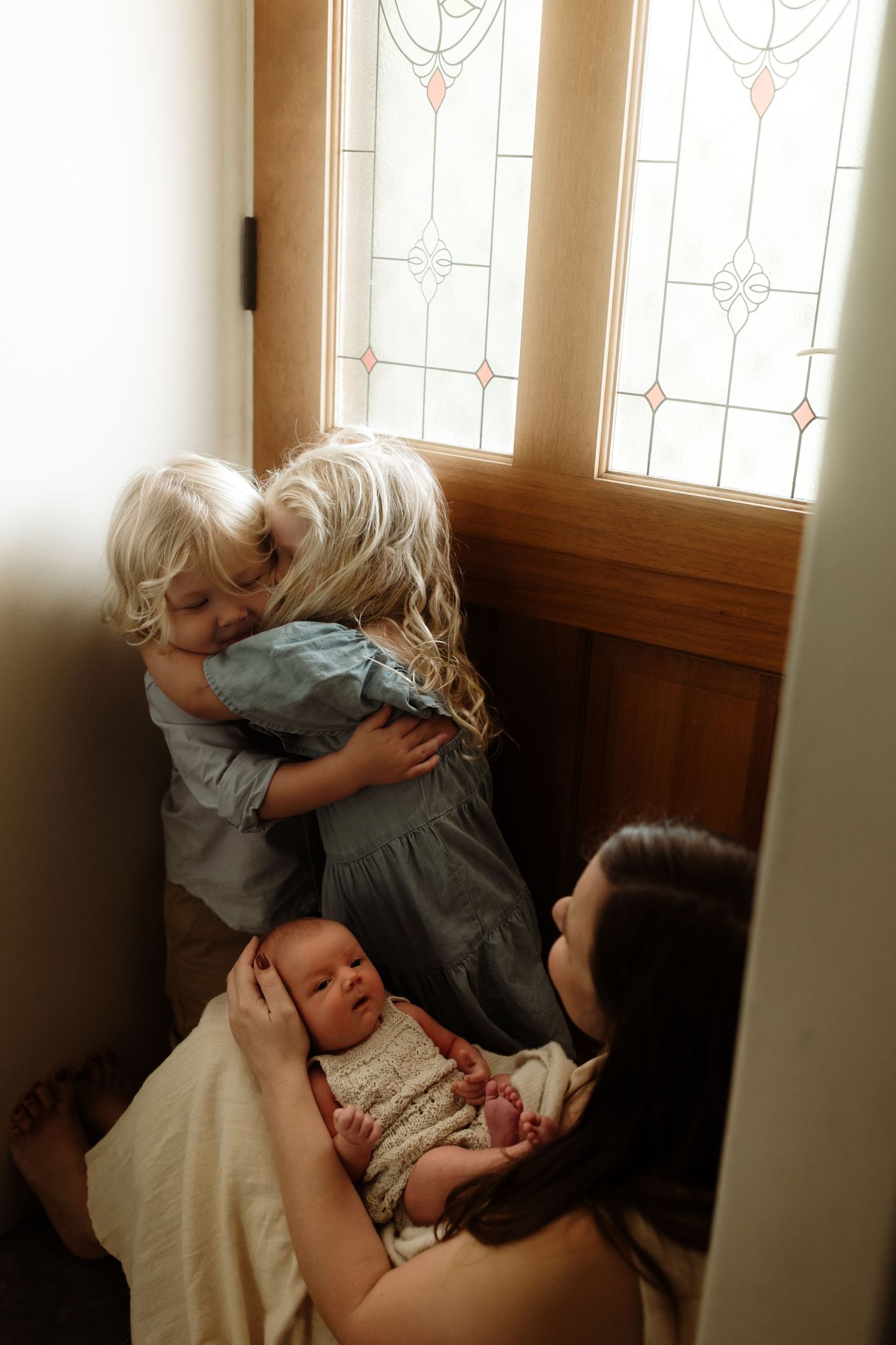 Intimate family moment captured near window with stained glass details.