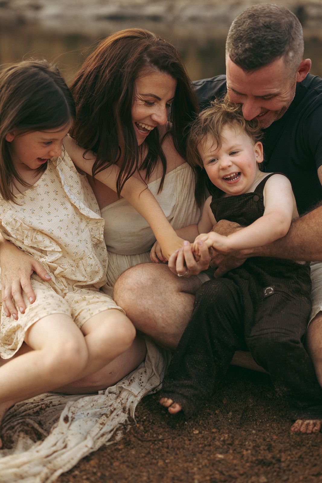 A family shares a joyful candid moment together sitting outside in casual attire.