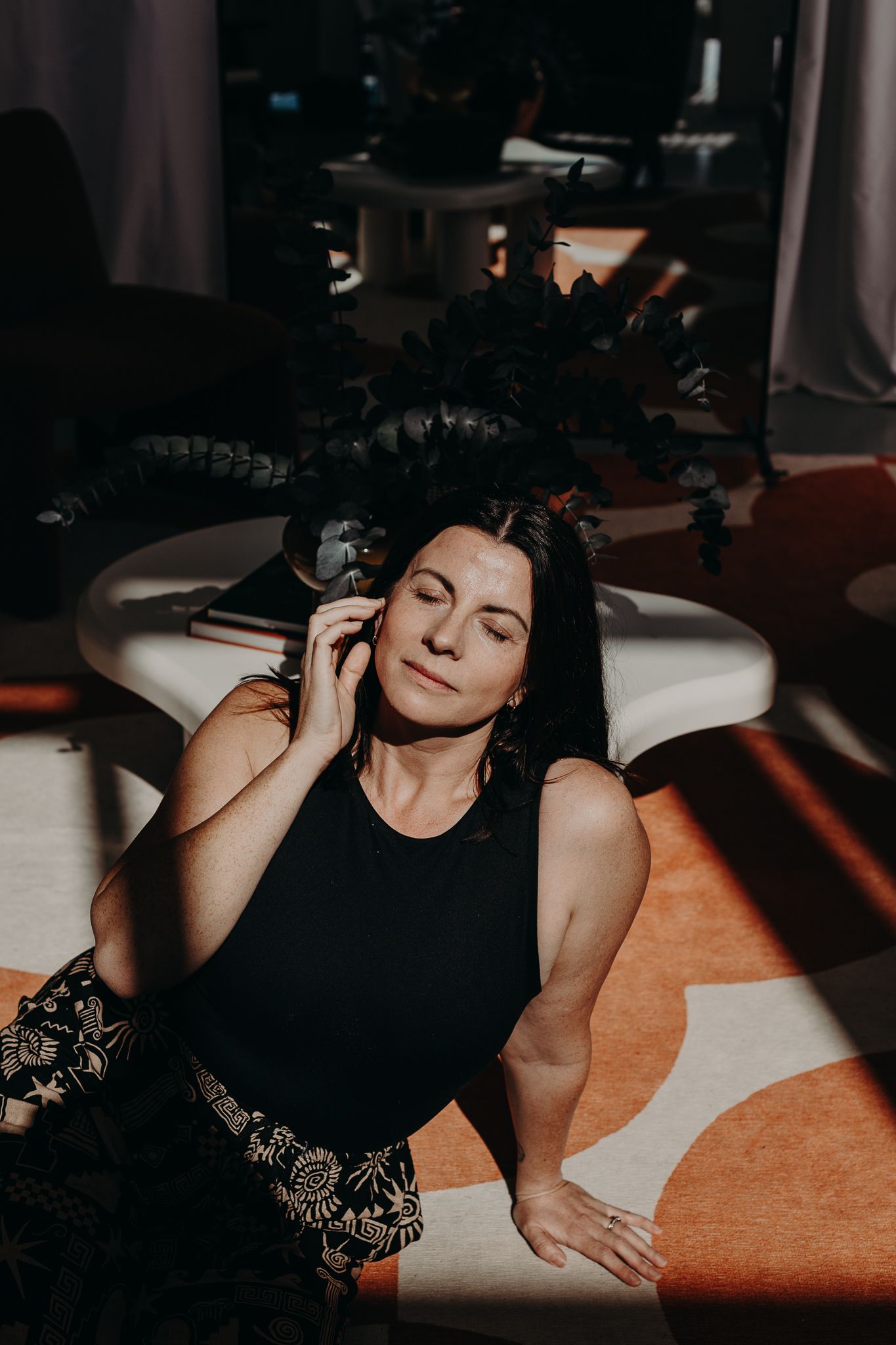 A relaxed woman in a black tank top lies on a white surface in moody lighting.