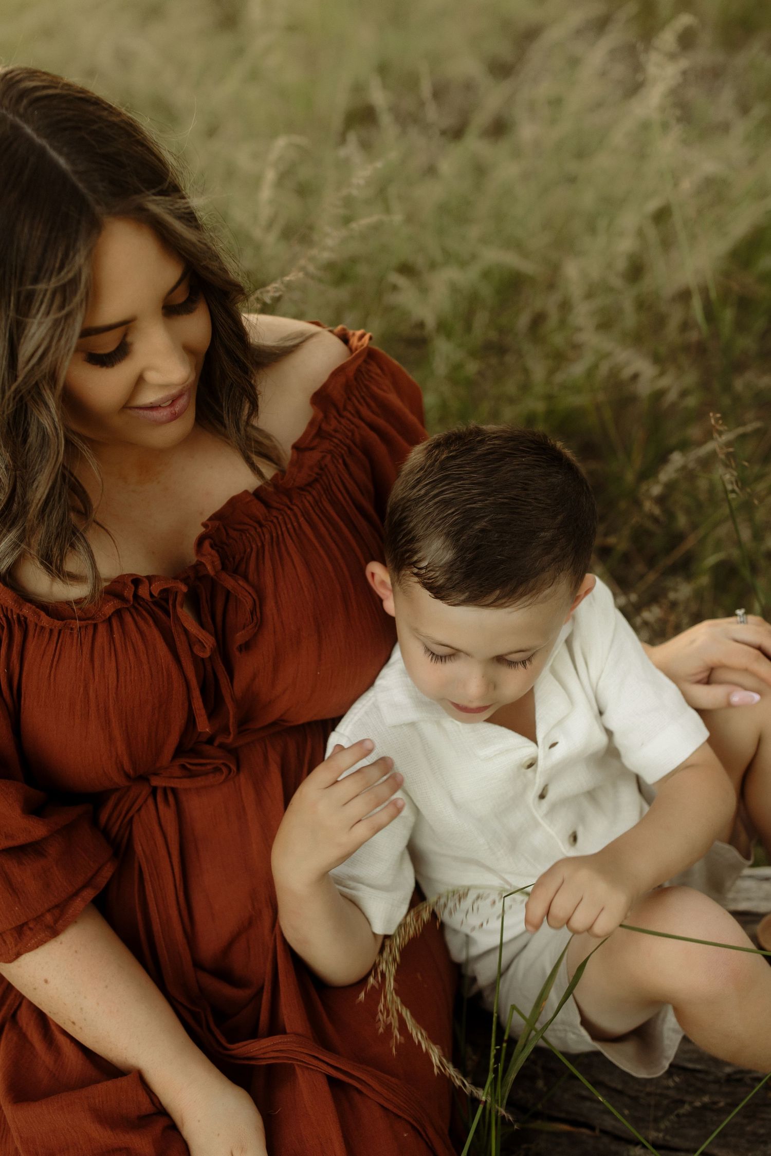 Candid moment between parent and child sitting in tall grass wearing red and white.