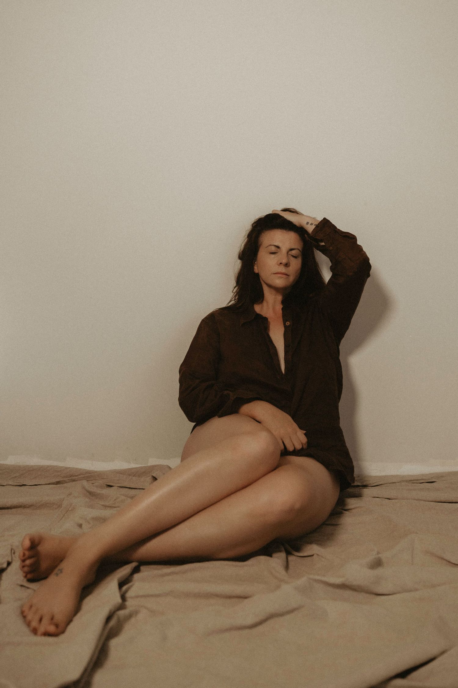 Woman in dark shirt poses artistically on beige backdrop.