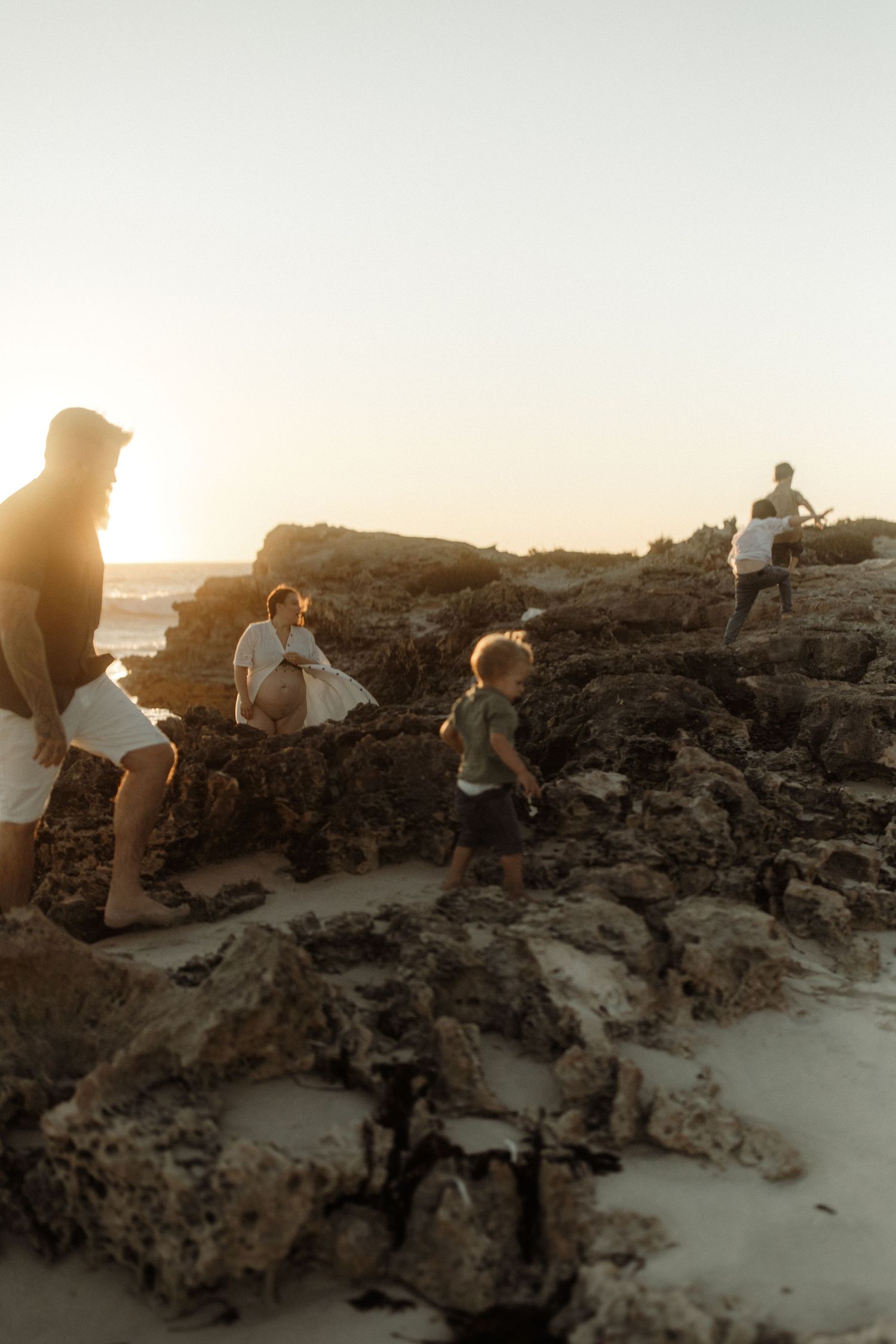 People exploring rocky coastal areas during golden hour sunset at the beach with warm atmospheric lighting.