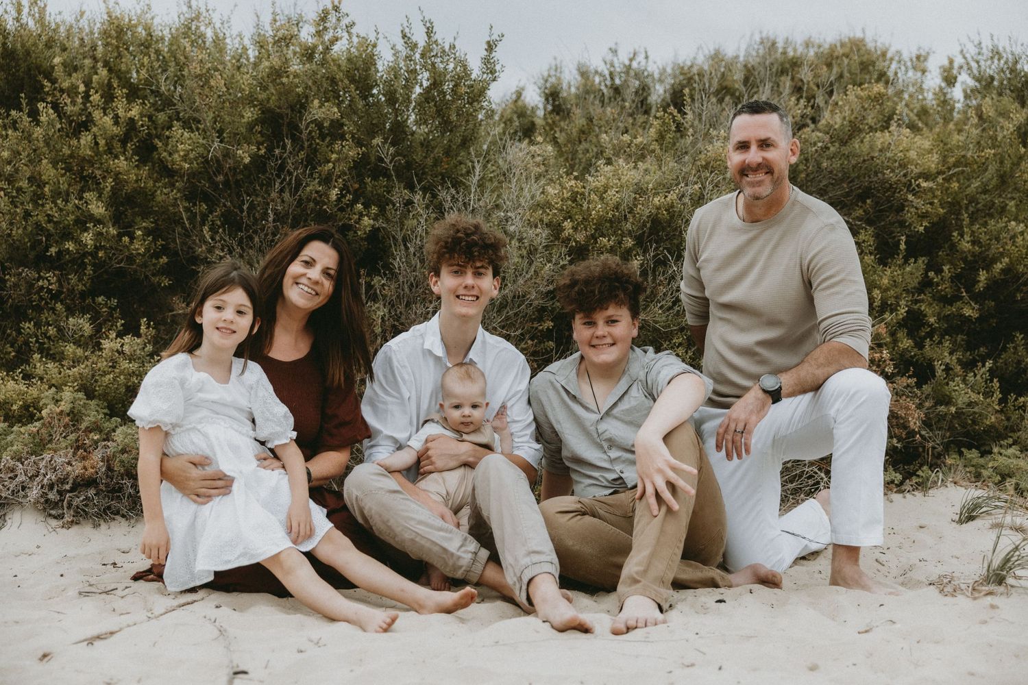Family group sitting together outdoors for casual portrait on sandy ground.