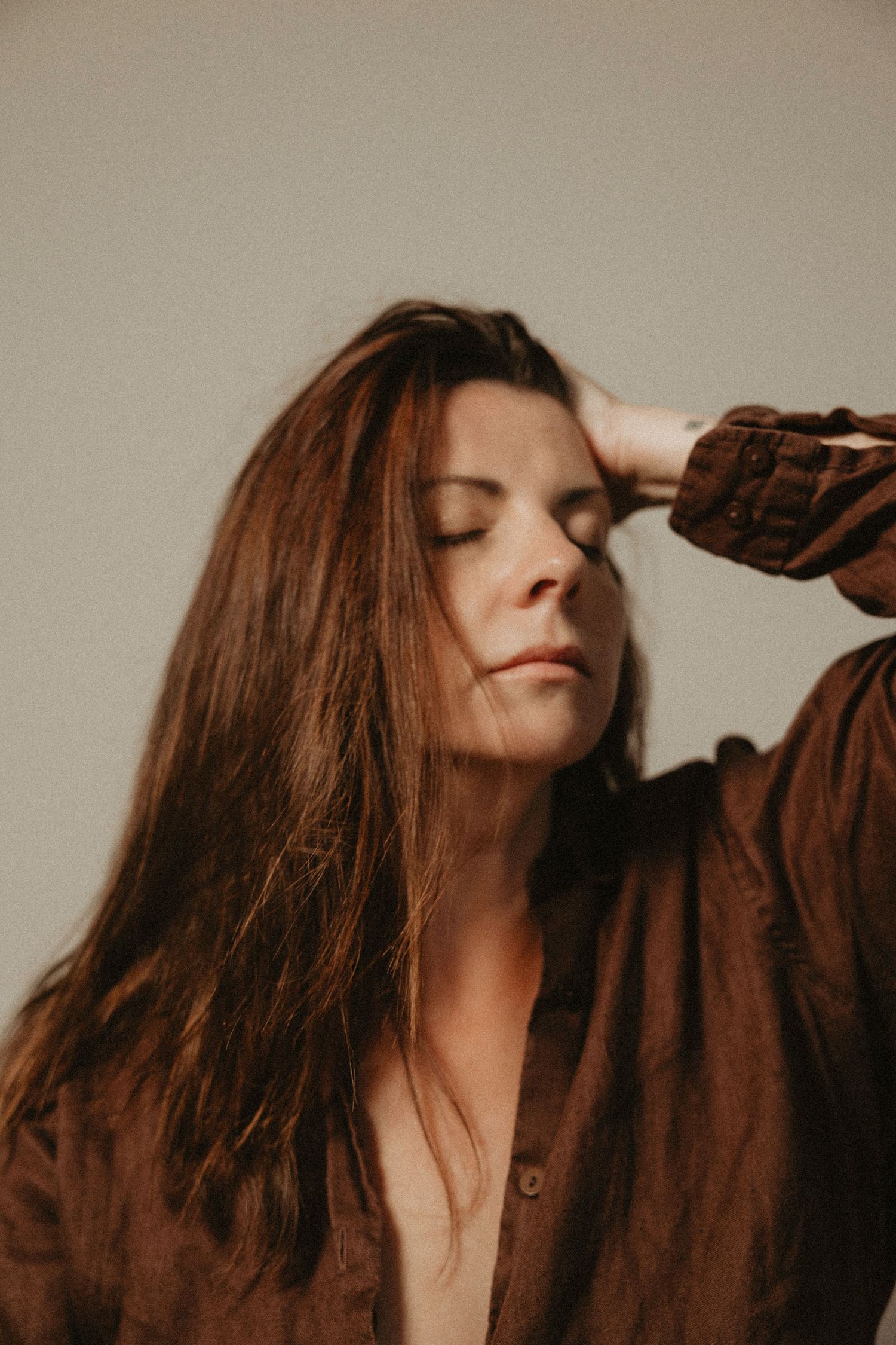 Moody portrait of someone with long brown hair in a brown shirt with eyes closed in contemplative pose. Courtney Healy Photography