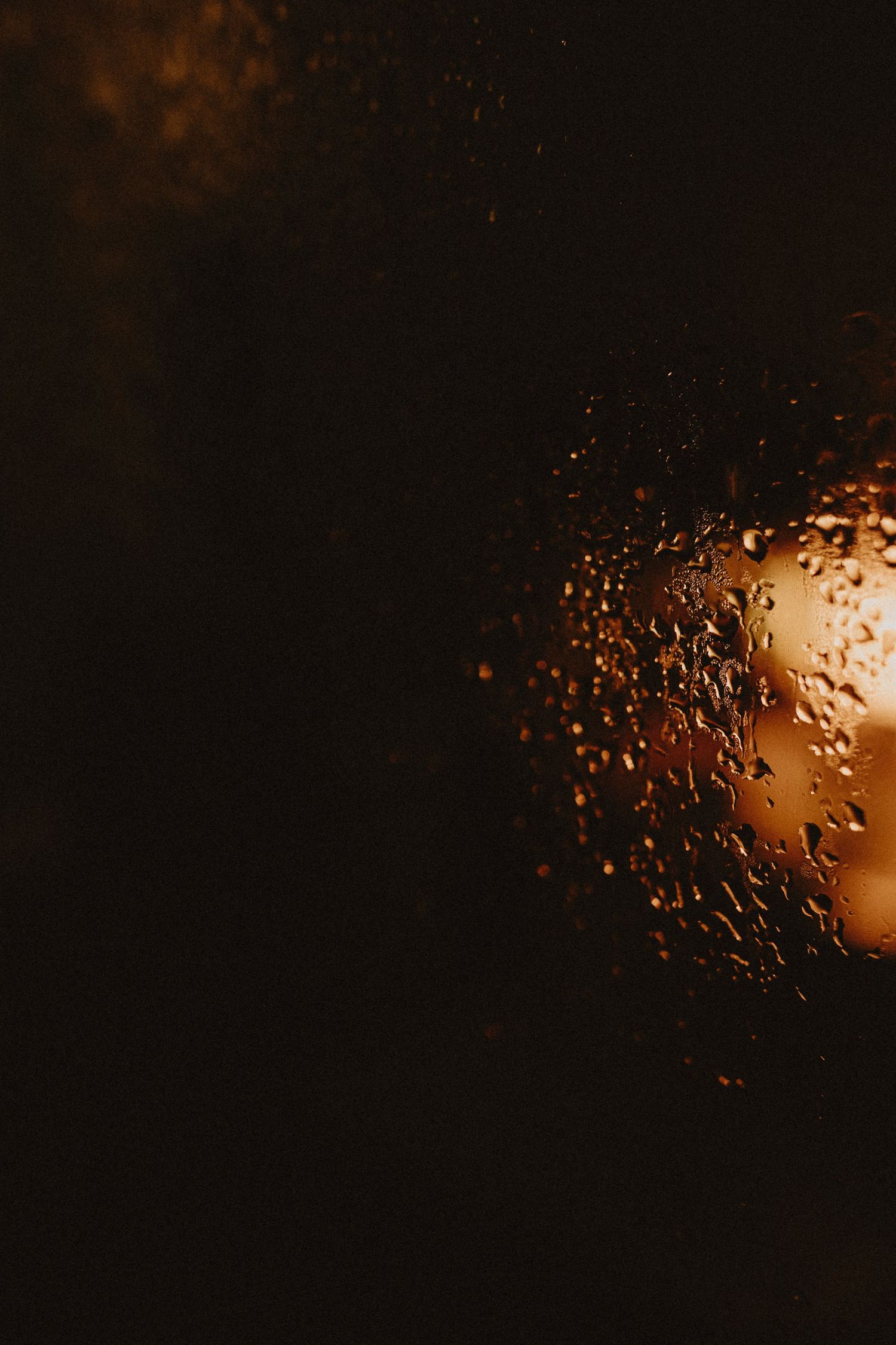 Water droplets on glass surface with warm glowing light in the dark background.