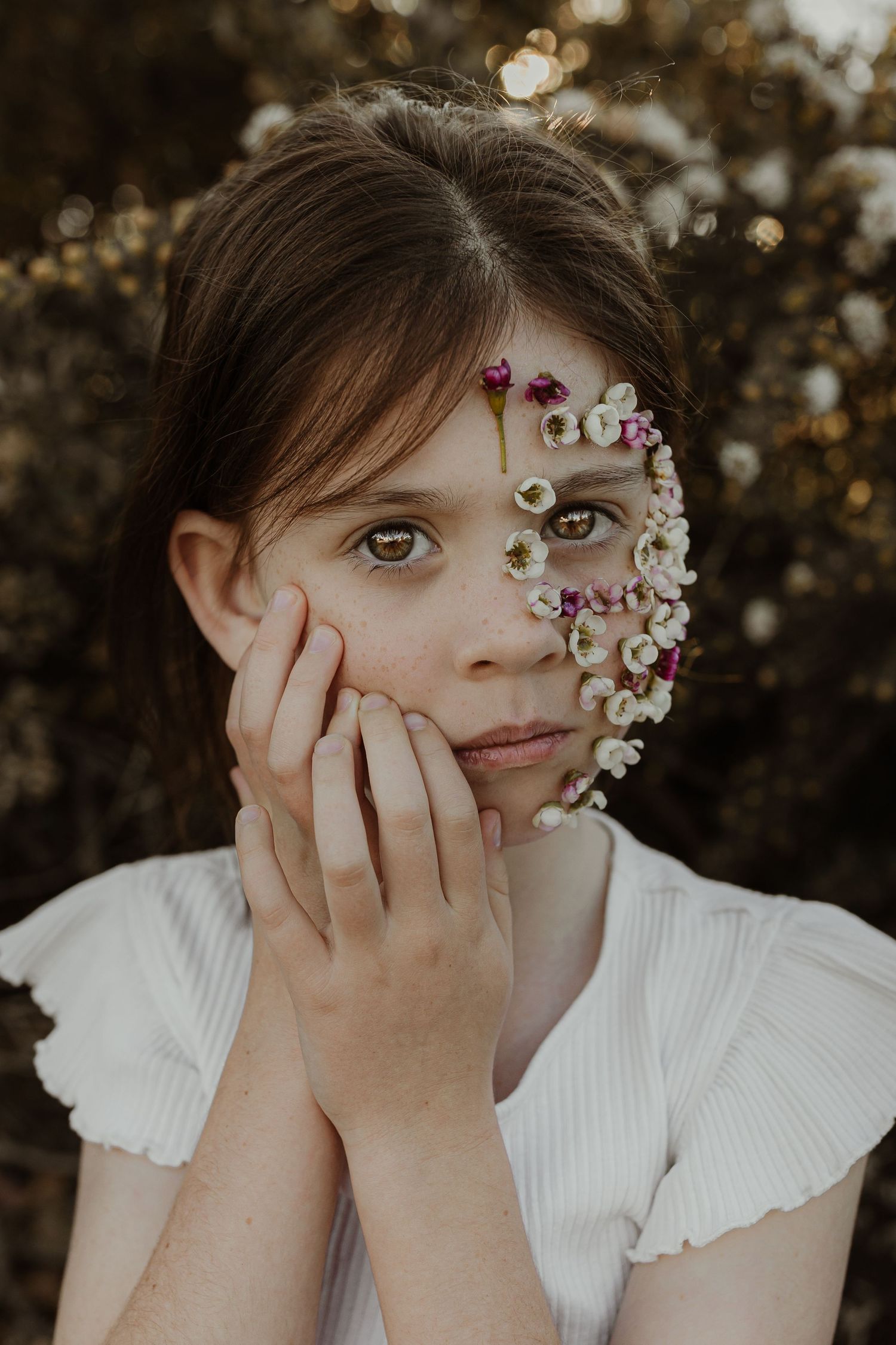 Artistic portrait featuring delicate flowers arranged around one side of the face against a warm bokeh background. Autistic child
