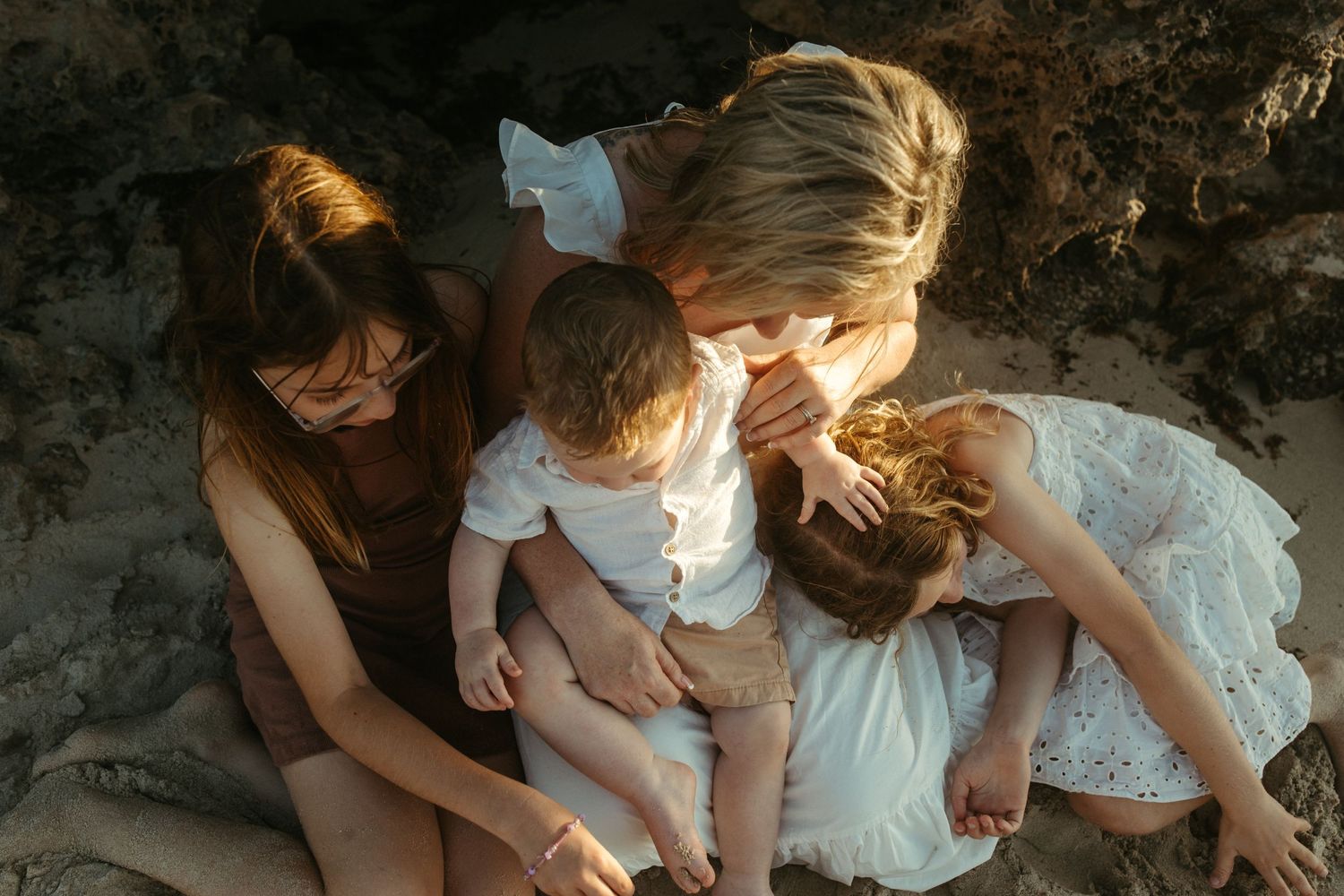 Family sitting together on sandy beach during golden hour near rocky cliffs.