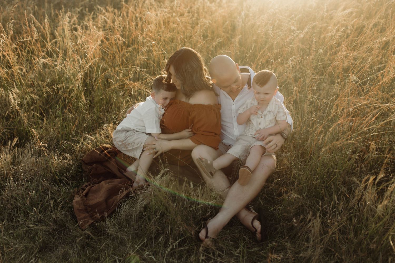 Family sitting together in tall grass during golden hour sunset.