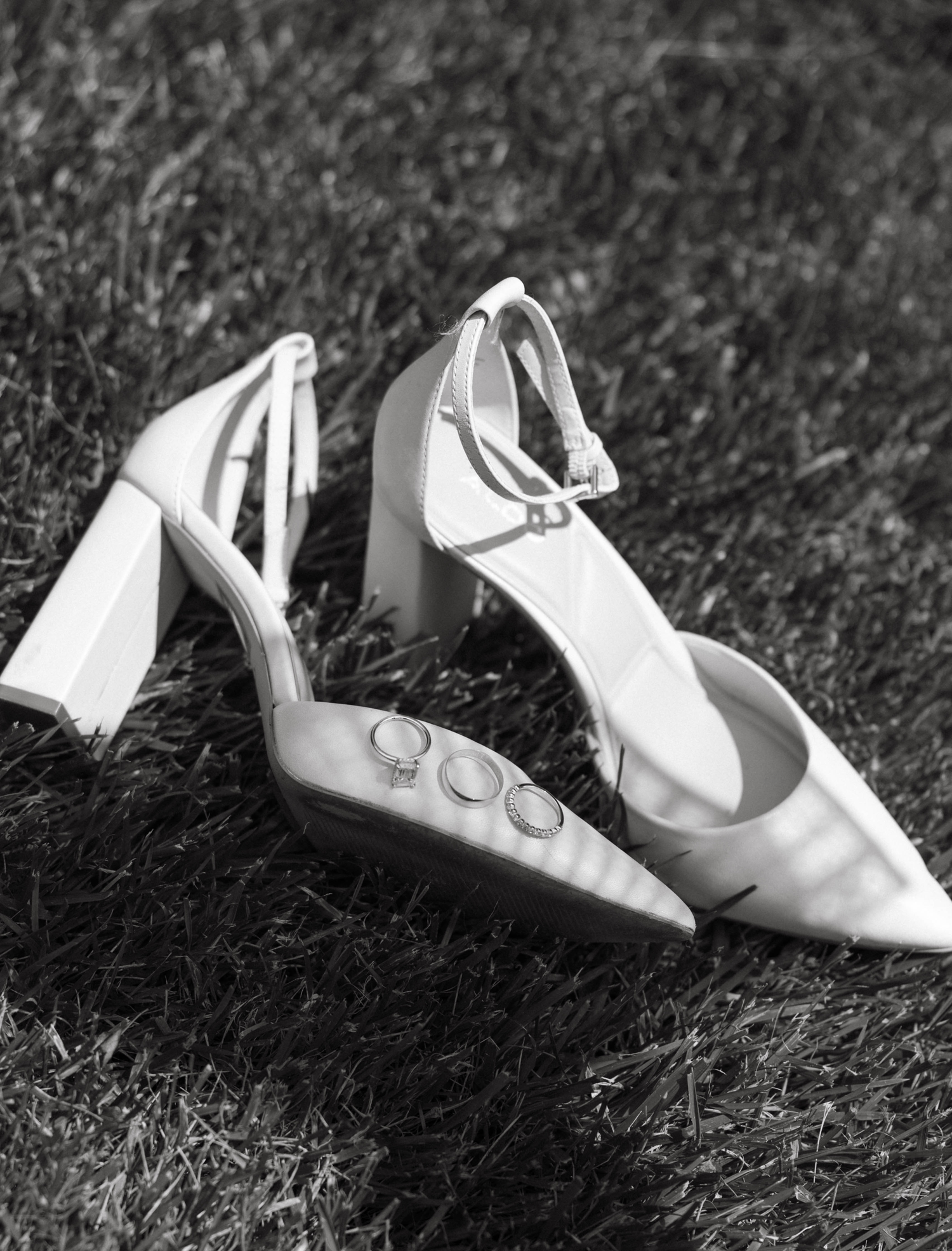 A sequence of white baby shoes arranged in a row on grass, shown in black and white photography.