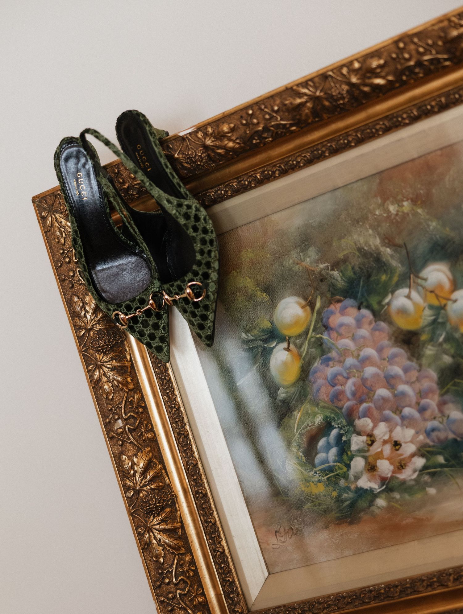 A vintage ornate gold frame with floral artwork hangs on a wall with a black headphone resting on its corner.