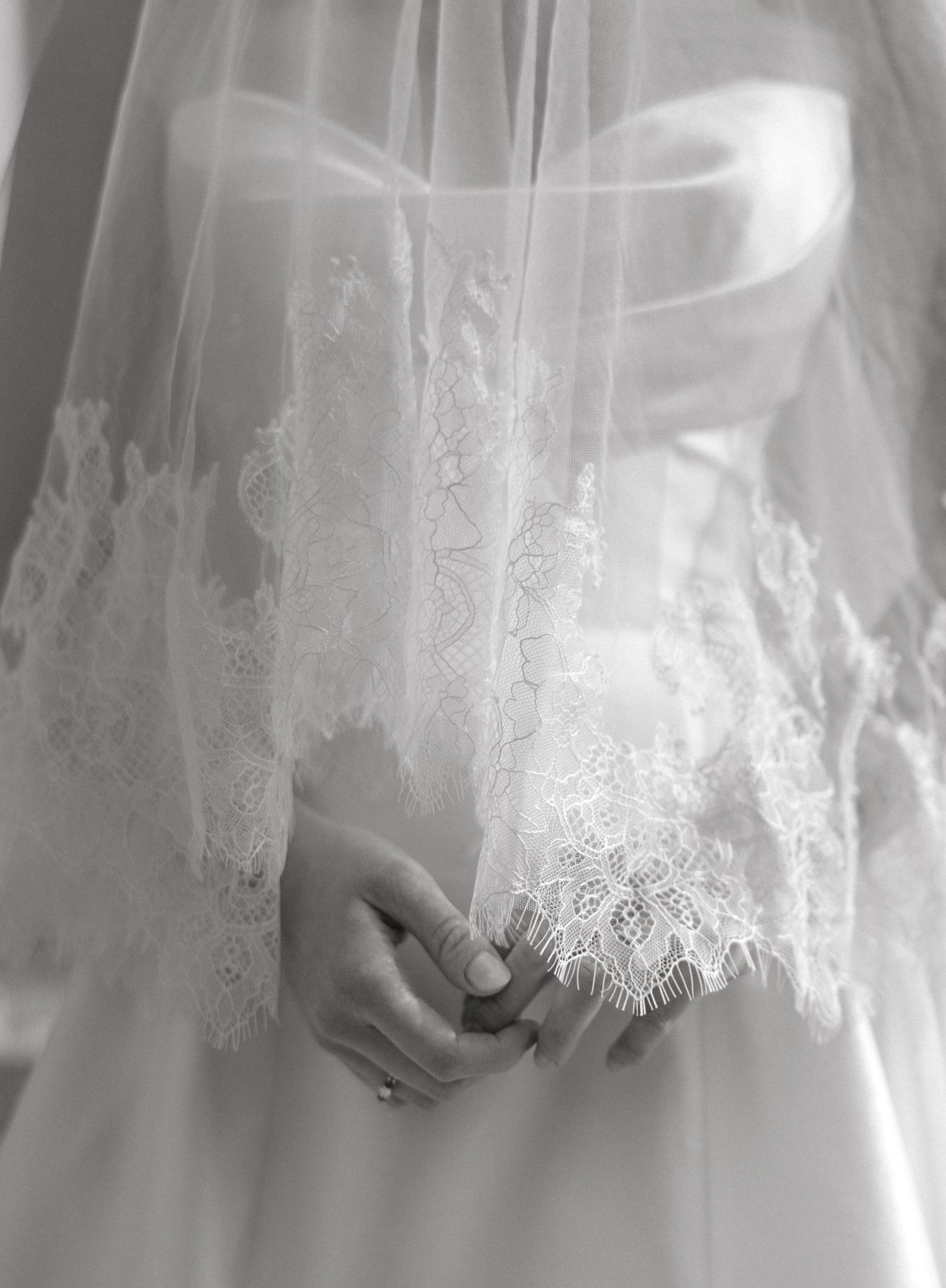 Close-up detail of delicate white lace trim on a wedding dress with intricate floral patterns and scalloped edges.