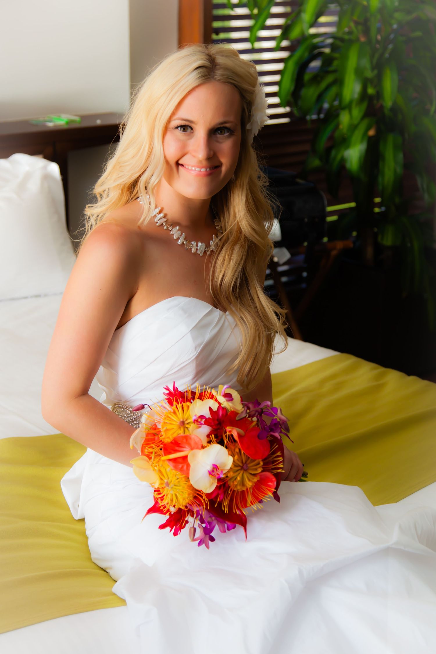 Wedding portrait of blonde bride in white dress holding vibrant orange and pink tropical bouquet at the Mauna Lani Bay Hotel.
