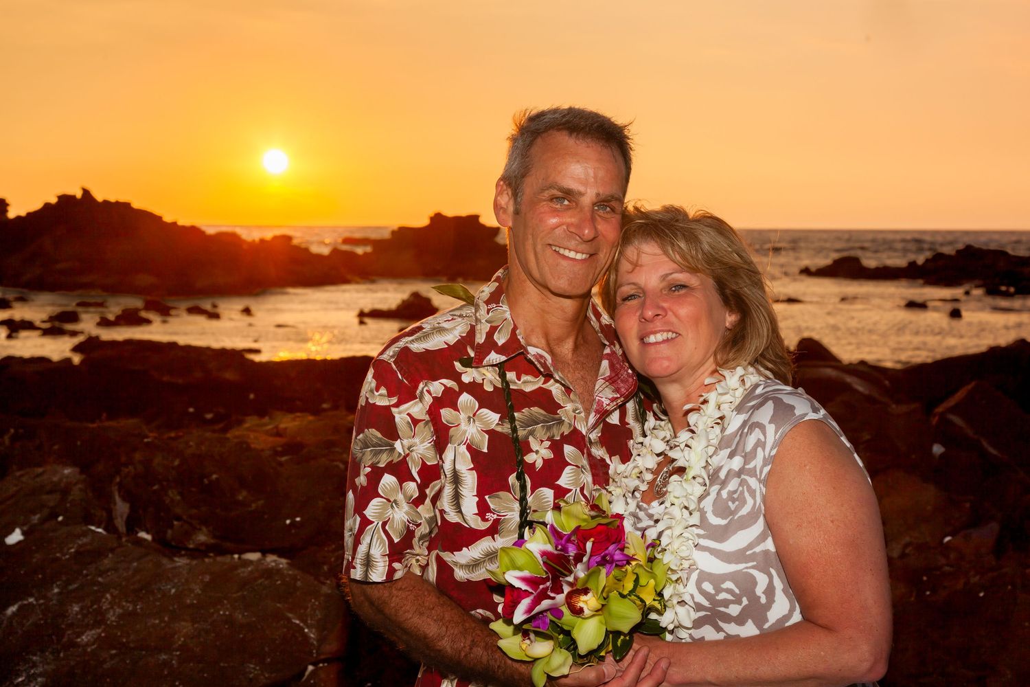 Portrait of a couple in Hawaiian attire posing at sunset at Kikaua beach in Kailua-Kona, Hawaii.
