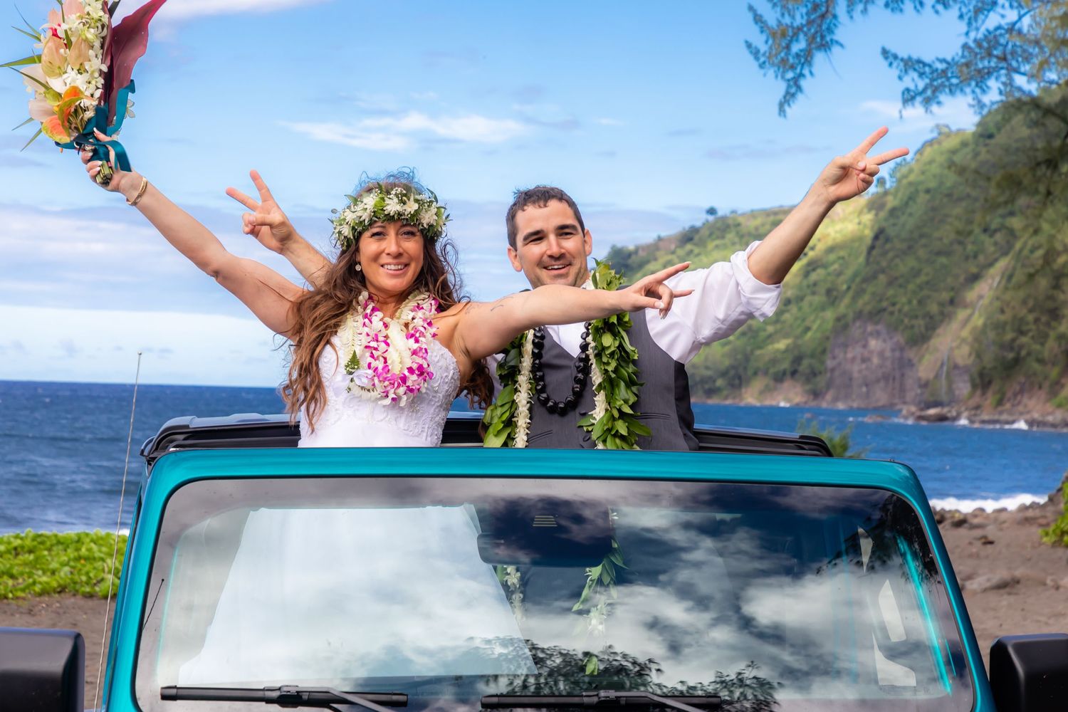 Joyful newlyweds in leis celebrate atop a teal convertible with Hawaii's ocean cliffs backdrop.