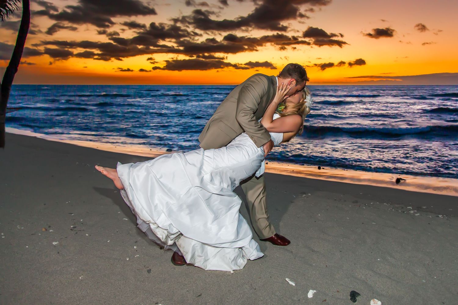 Romantic beach sunset wedding dip pose silhouetted against orange sky at the Mauna Lani Bay Hotel in Kona.