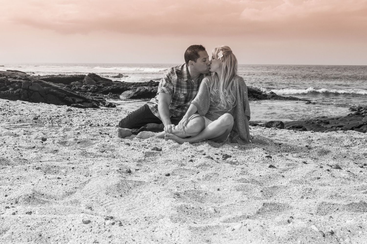 A romantic couple lies together on a sandy Kailua Kona beach, capturing a beautiful sunset engagement photo session.