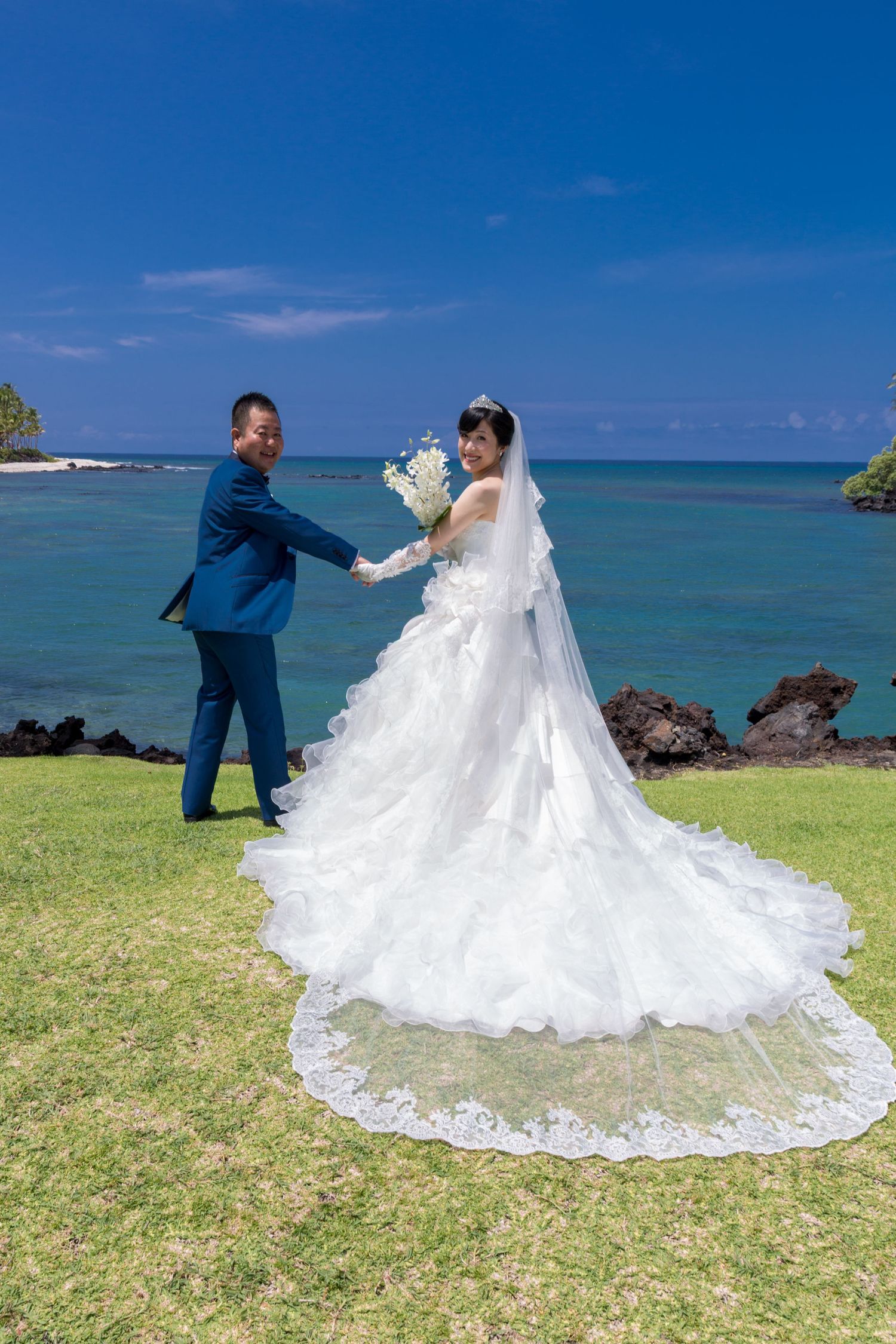 A couple poses for wedding photos on a scenic Hawaiian coast with blue ocean and sky at the Hilton Waikoloa Village near Kailua Kona.
