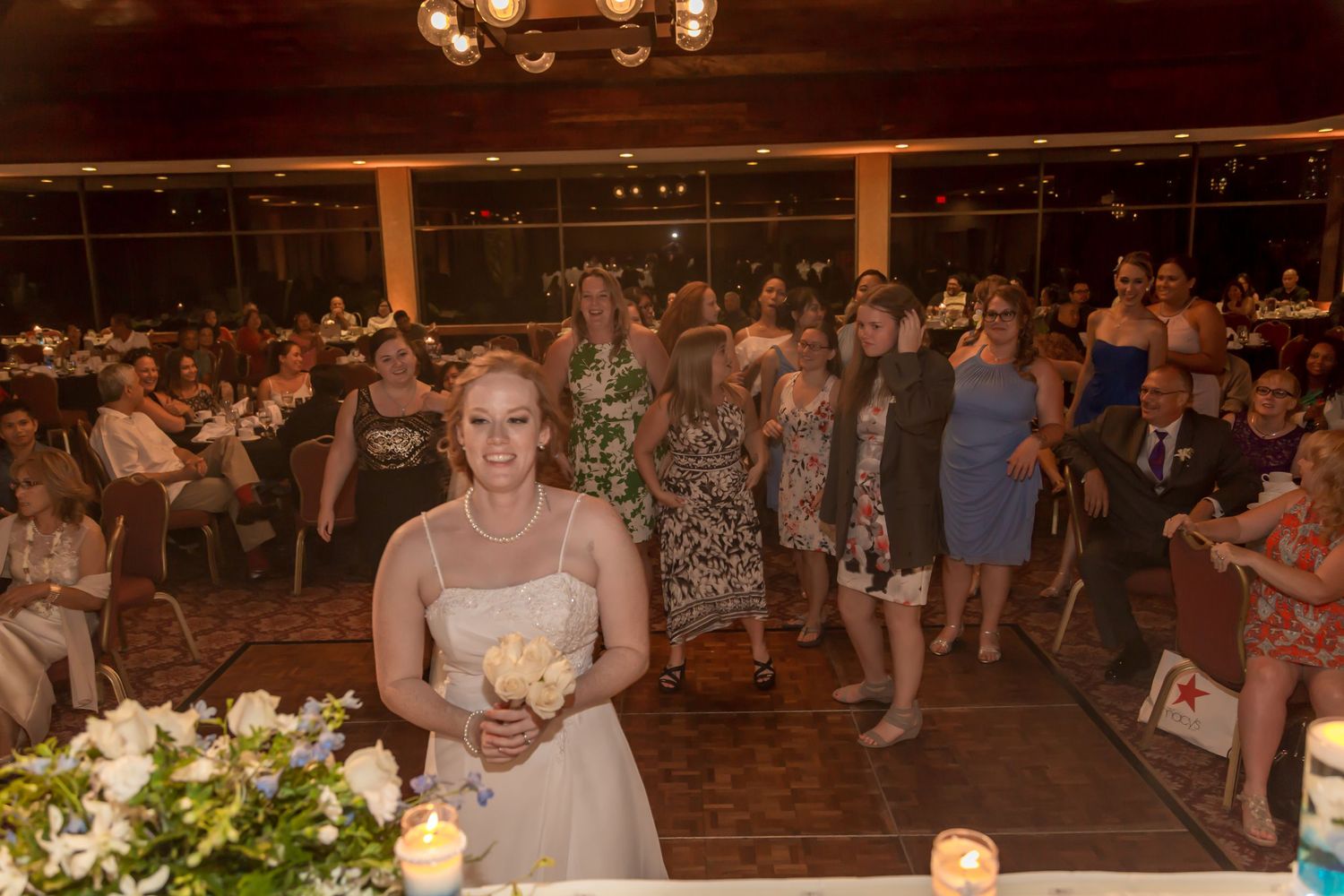 Bride prepares to toss bouquet to excited guests at elegant indoor wedding reception.
