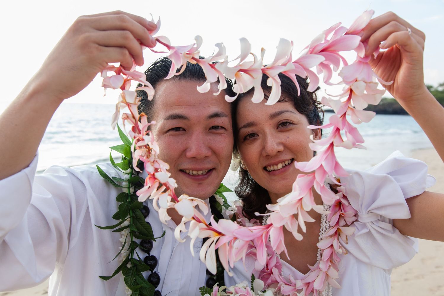 A bride and groom in beautiful leis during their candid beach elopement in Kailua Kona, Hawaii.