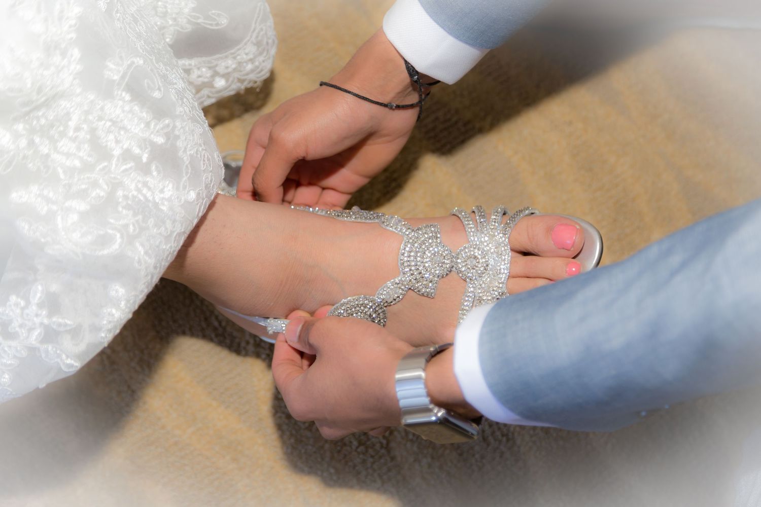 Groom fastening ornate crystal barefoot sandal jewelry on bride's foot at wedding ceremony.
