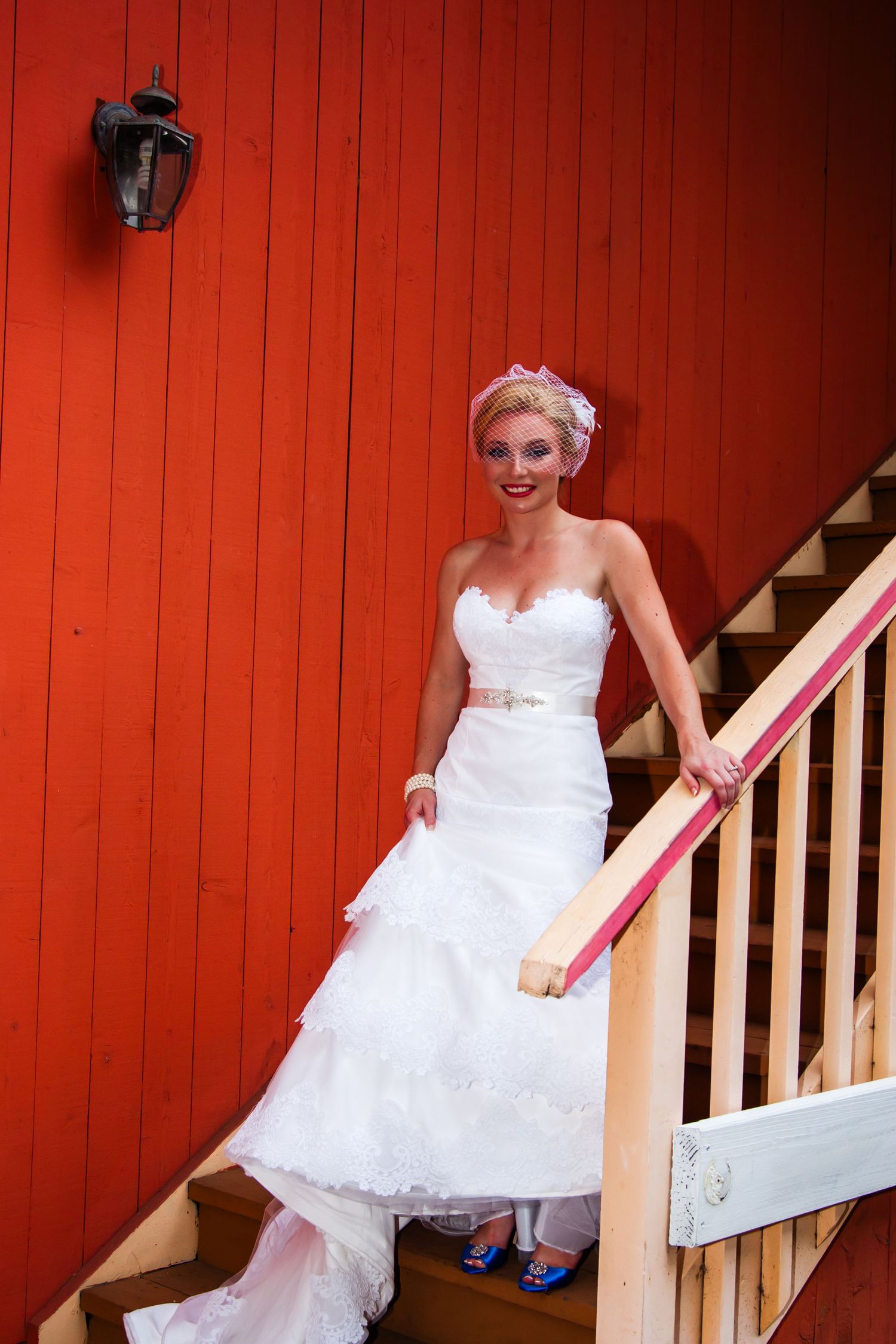 A bride in a strapless wedding gown stands on red wooden stairs wearing blue shoes in a wedding on a private state at Kailua Kona.