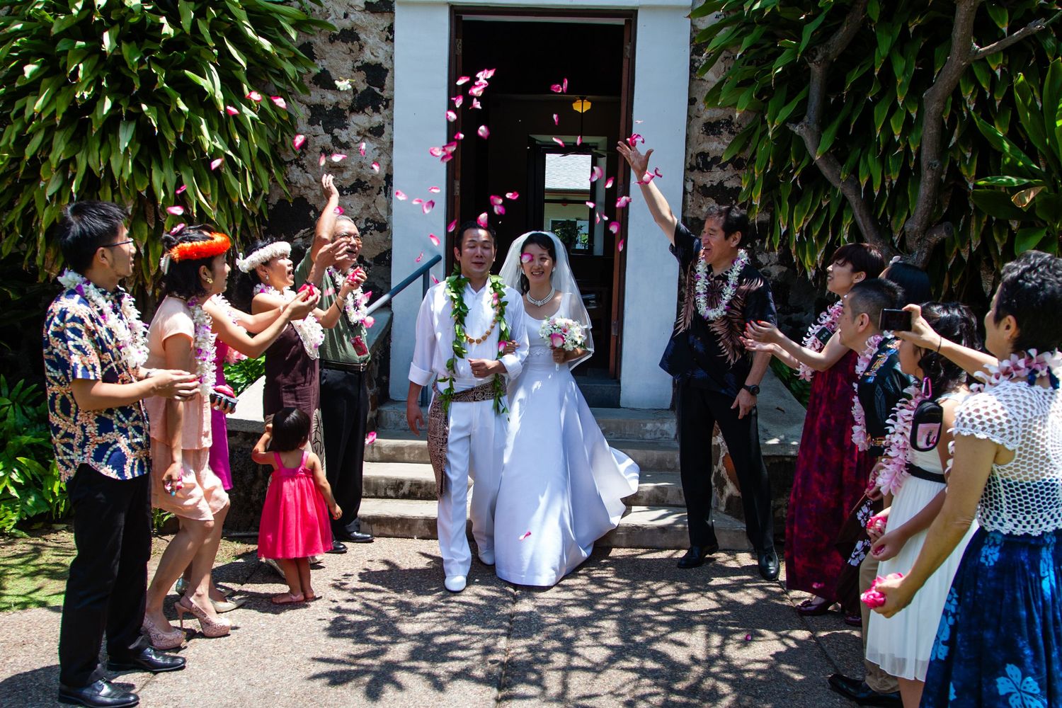 Newlywed couple exits church as guests toss flower petals in a tropical Hawaiian wedding celebration.