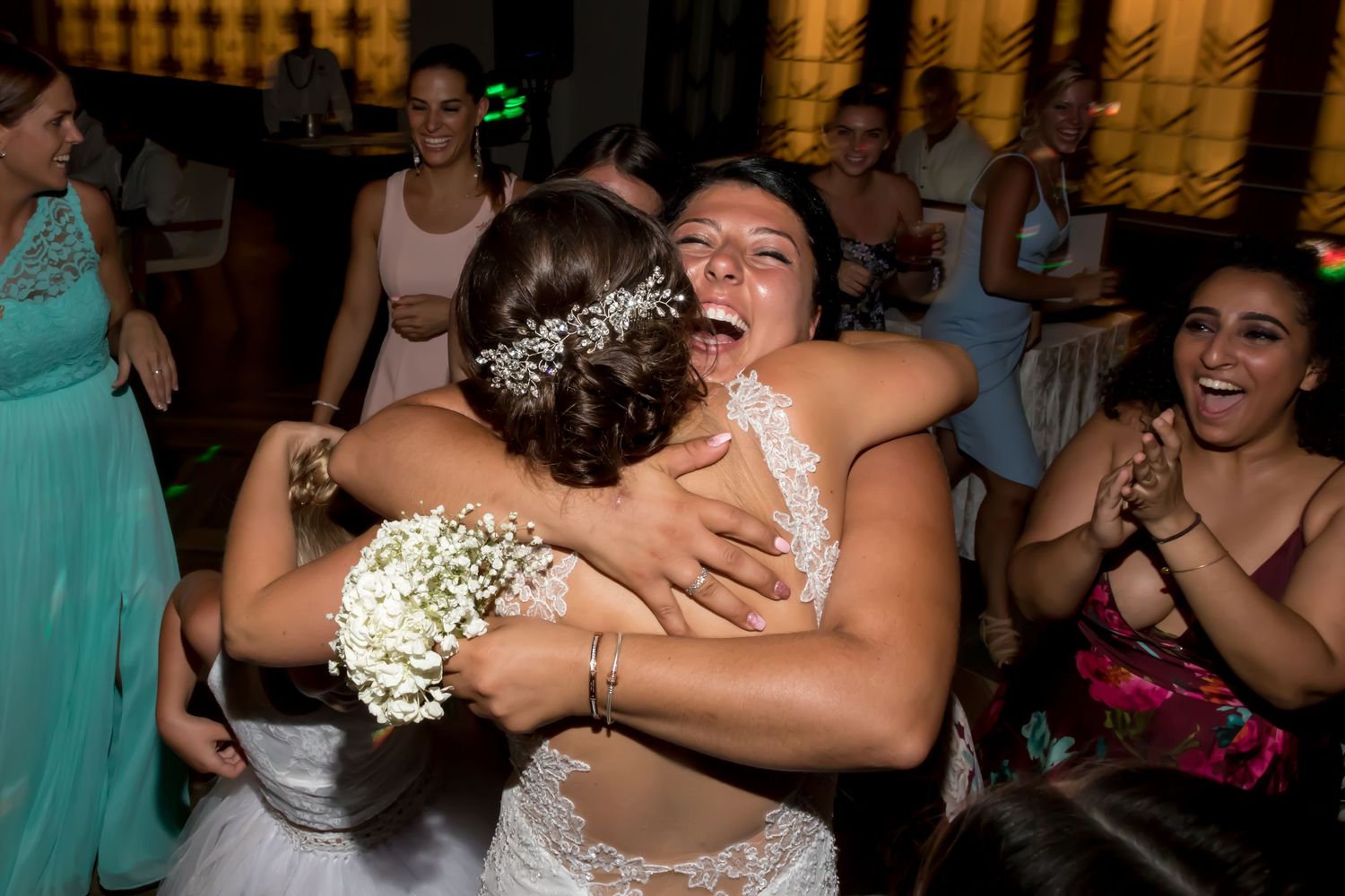 Two brides sharing an emotional hug on the wedding dance floor surrounded by celebrating guests.
