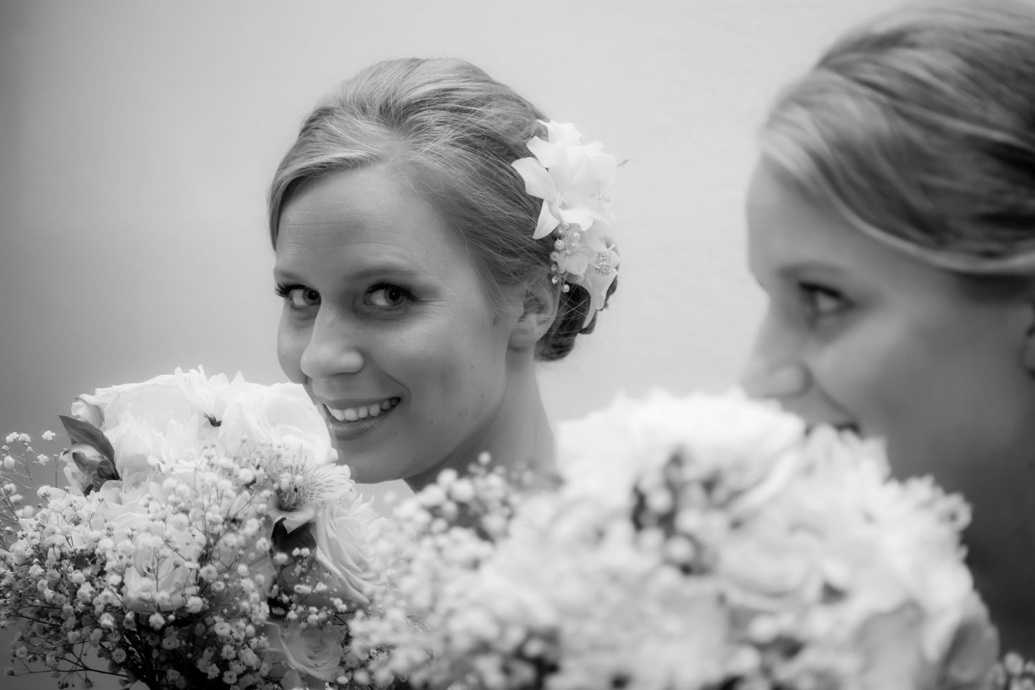 A bride reflects against a mirror holding a bouquet of white flowers in a black and white wedding photo.