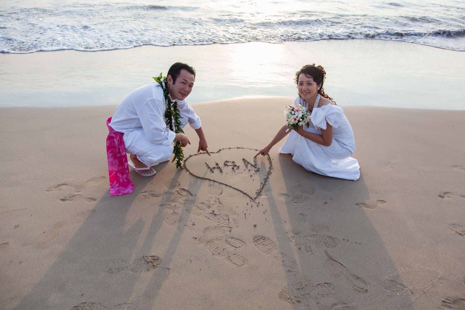 A newly engaged couple draws a heart in the sand during a candid engagement photo session in Kailua Kona, Hawaii.