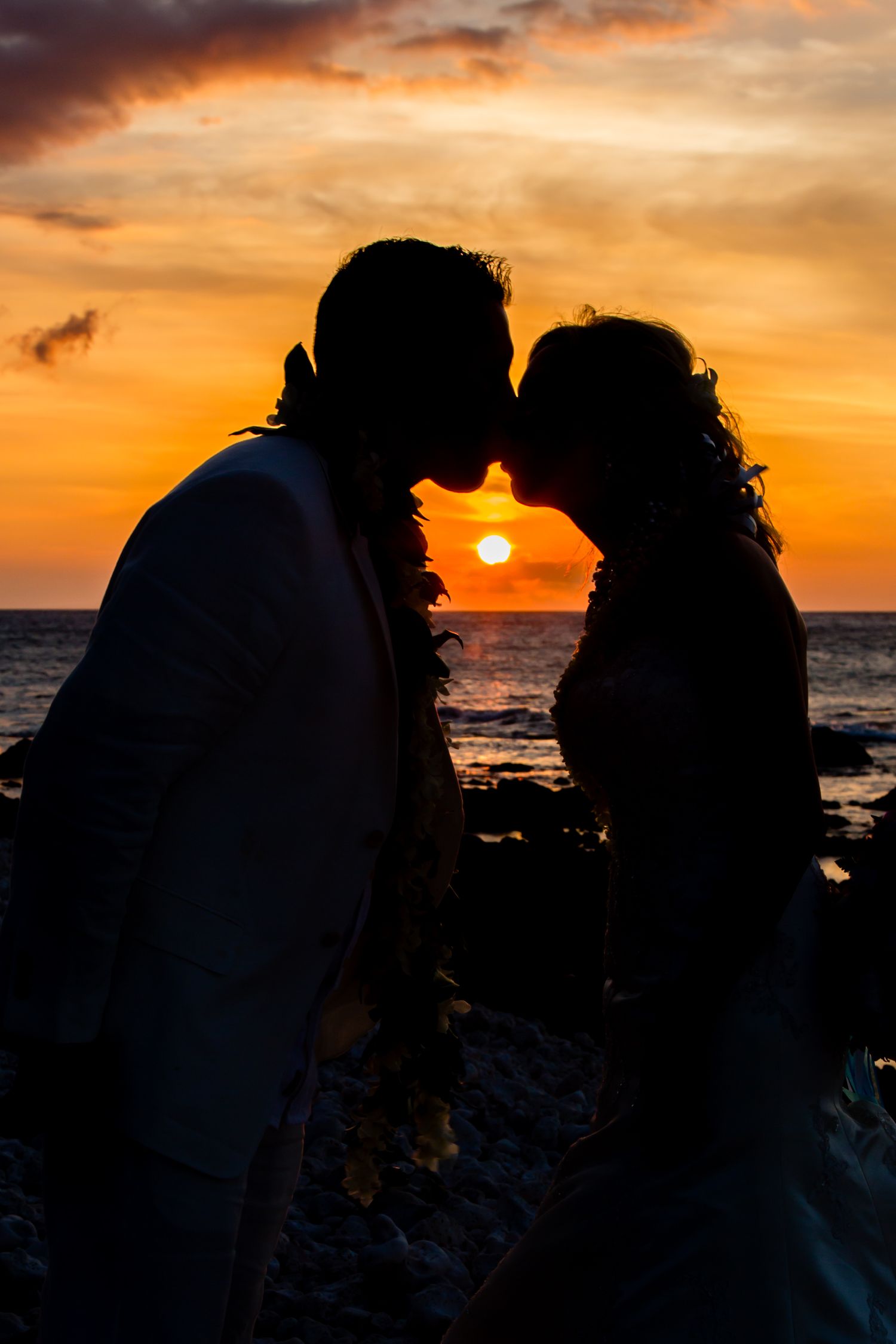 A romantic silhouette of a couple against a dramatic orange and purple sunset over the ocean.