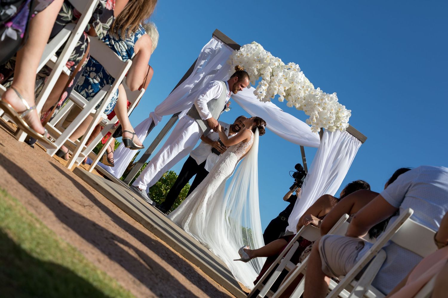Couple exchanging vows at an outdoor wedding ceremony under a white floral arch.