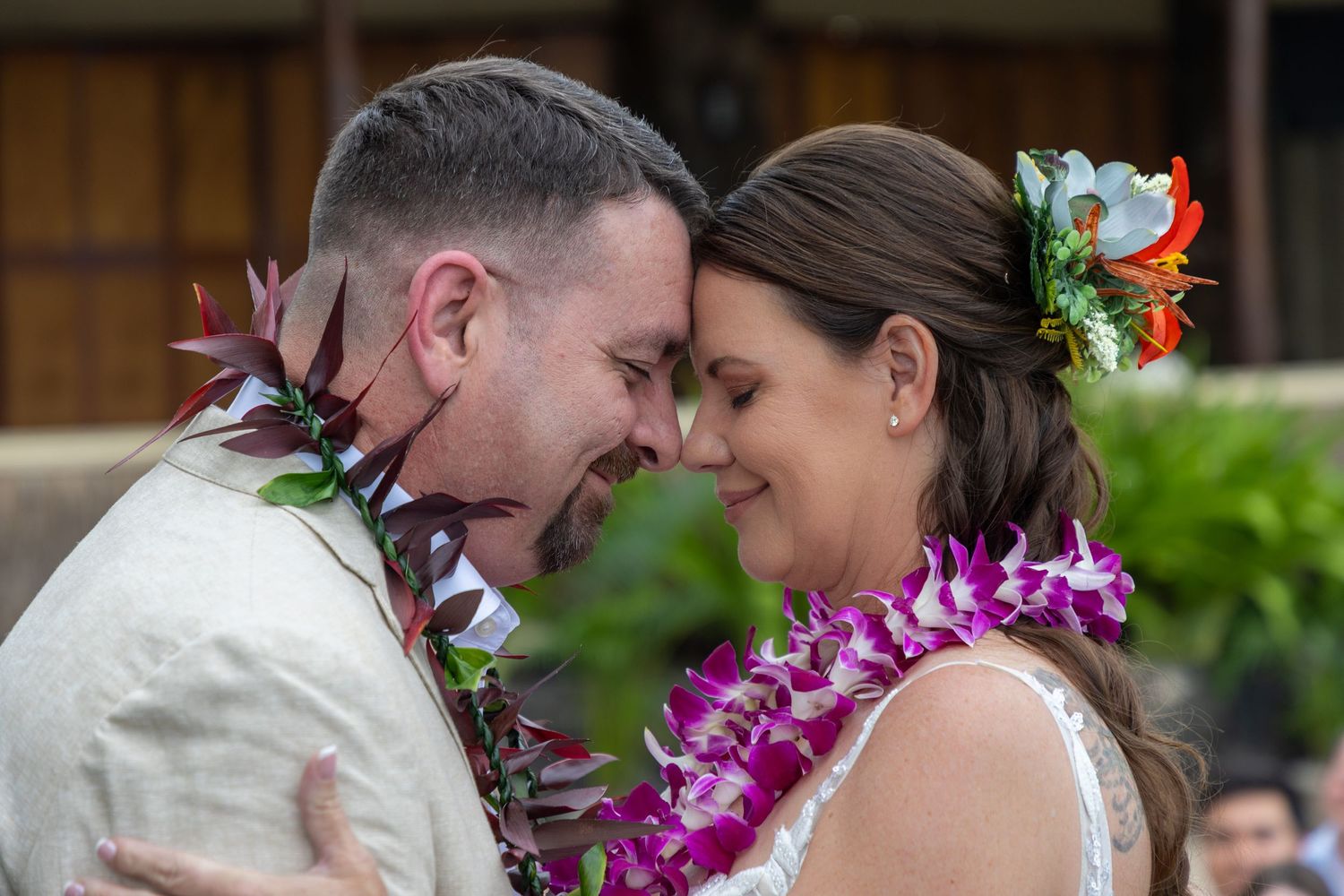 Couple in floral leis sharing an intimate moment at a Hawaiian wedding ceremony.