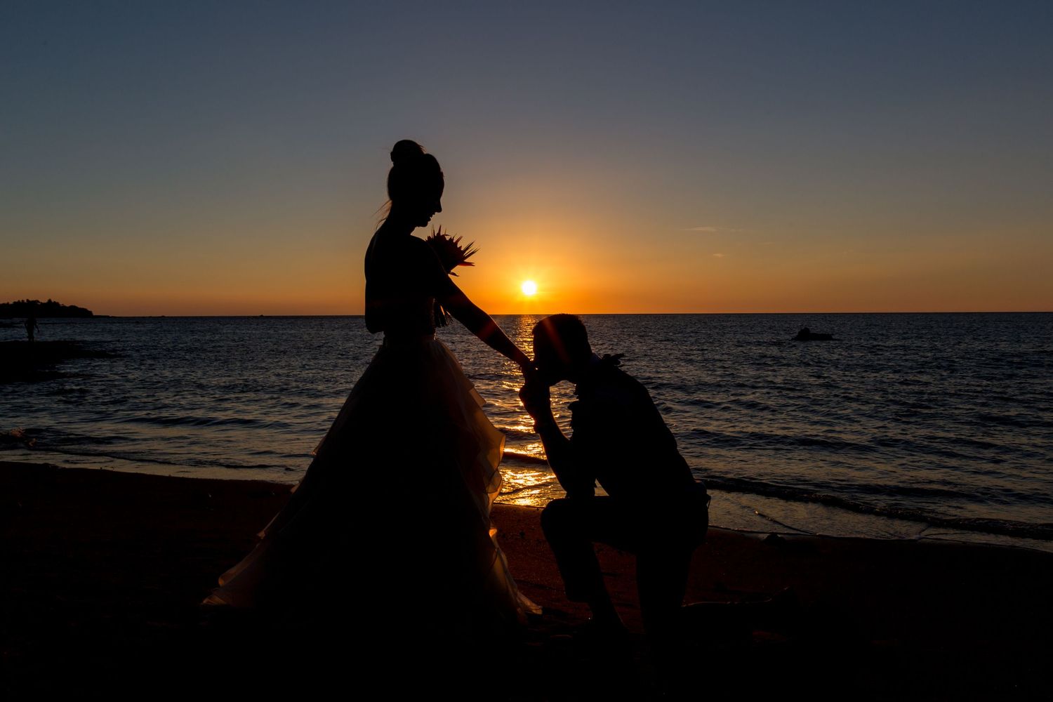 Silhouette of a couple in wedding attire sharing a romantic moment on the beach at sunset.