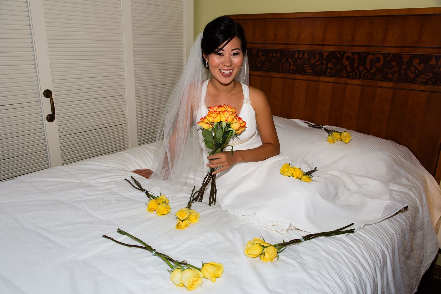 A bride sitting on a bed decorated with yellow flowers holds a vibrant bouquet in Kailua Kona